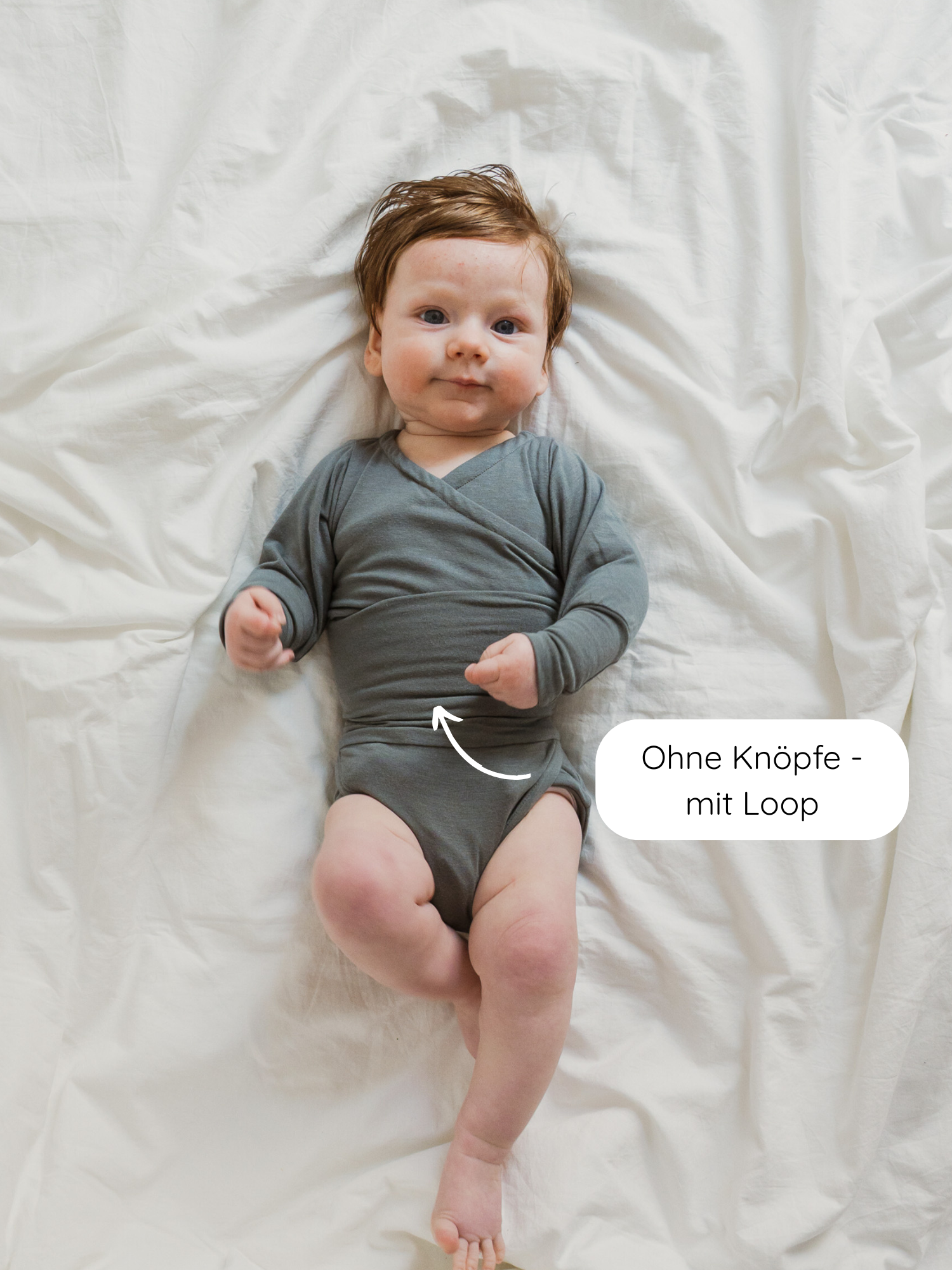 Ein Baby trägt den Loopbody Kaschmir-Mix - Taube, einen grauen, langärmeligen Wickelbody ohne Knöpfe, der mit einem praktischen Loop für einfaches An- und Ausziehen ausgestattet ist.
