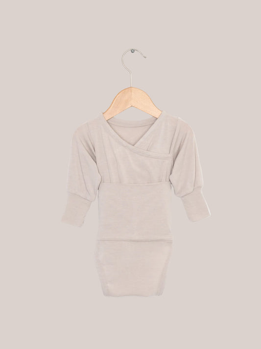 Loopbody Cashmere Blend – Sand: A baby bodysuit without buttons on a wooden hanger. The soft, long-sleeved bodysuit features a special loop for easy dressing and provides extra warmth. Baby starter essentials and a baby birth gift.