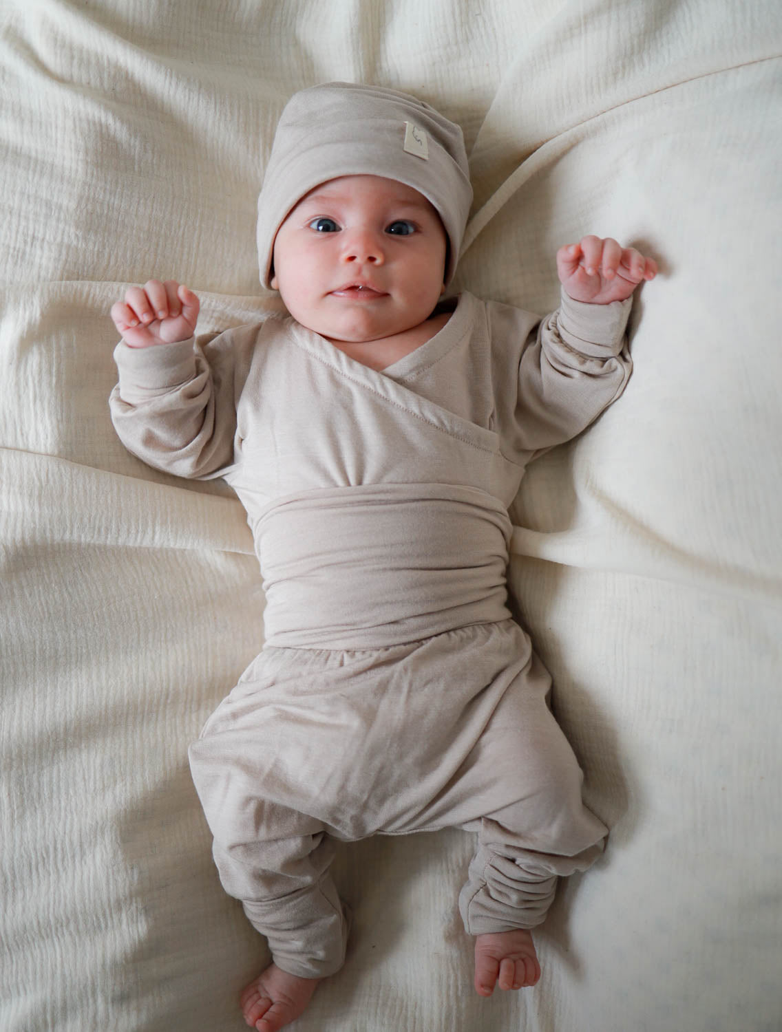 Baby auf Decke in Loopbody Kaschmir-Mix ohne Knöpfe, sandfarben, mit langem Ärmel und Loop um den Bauch, preisgekröntes, mitwachsendes Design von PETIT COCHON Berlin.