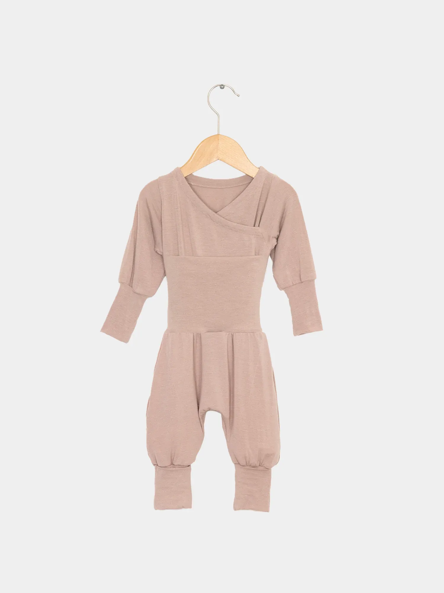 Loopstrampler Kaschmir-Mix - Puder: Ein taupefarbener, langärmeliger Babystrampler ohne Knöpfe, mit umklappbaren Bündchen und Wickelausschnitt, aus weichem Kaschmir-Micromodal-Mix, auf einem Holzbügel präsentiert.