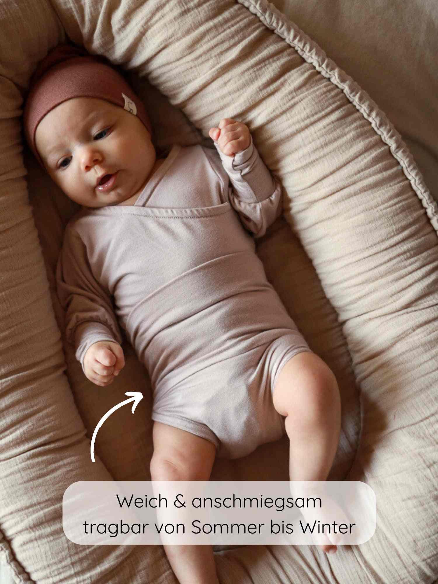 Ein Baby liegt in einem Loopbody Bambusviskose - Cremepuder, einem weichen, wachsenden Babybody ohne Knöpfe. Der Body ist beige und wird mit einer passenden Strickmütze getragen.