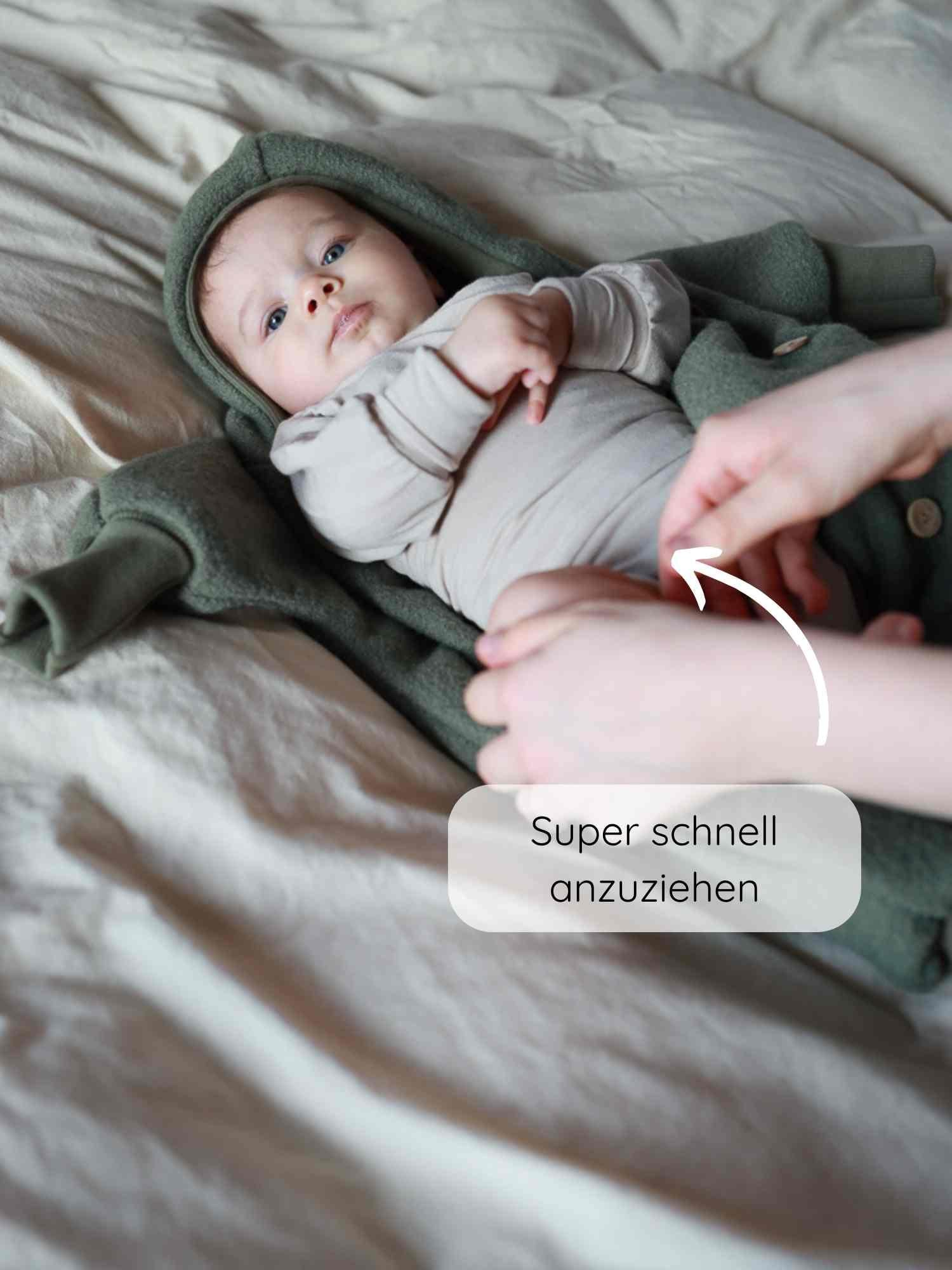 Ein Baby liegt auf einem Bett in einem Loopbody Bambusviskose - Cremepuder, während Erwachsene das Kleidungsstück schnell anziehen. Eine Grafik zeigt, wie einfach es zu schließen ist.