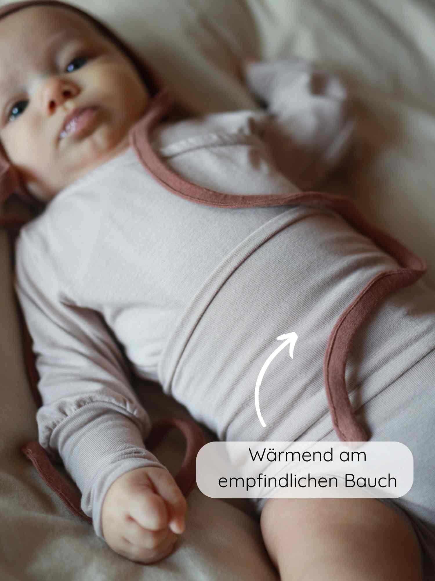 Baby in einem Loopbody Bambusviskose - Cremepuder, wickelstil, ohne Knöpfe, mit Fokus auf wärmespendender Funktion am Bauch. Ideal für empfindliche Babyhaut, atmungsaktiv und komfortabel für das ganze Jahr.