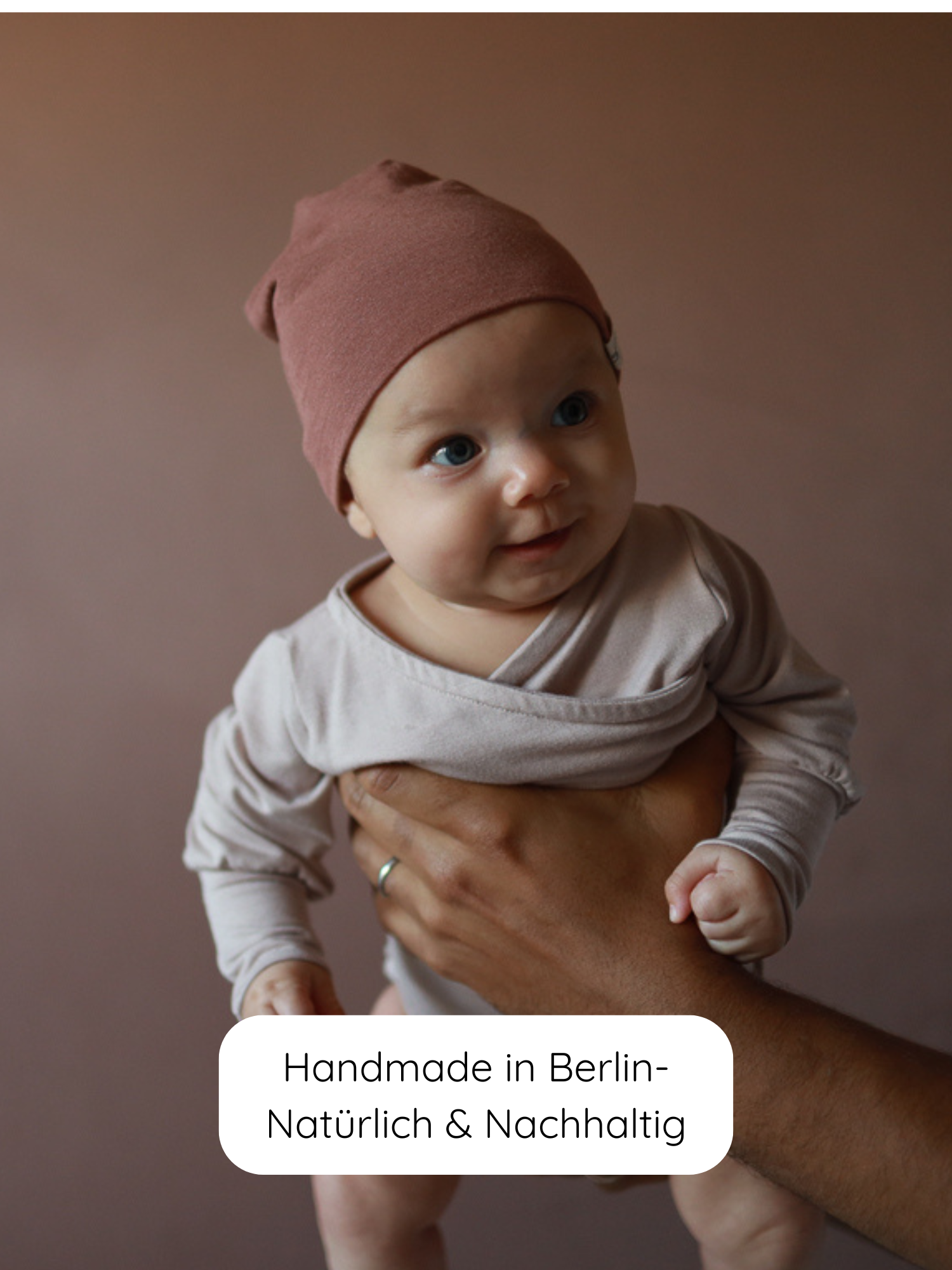 Ein Baby trägt einen Loopbody aus Bambusviskose - Cremepuder, gehalten von Erwachsenen. Der Body wächst mit, ist bequem, atmungsaktiv und nachhaltig, ideal für sanftes Wickeln und Schutz vor Zugluft.