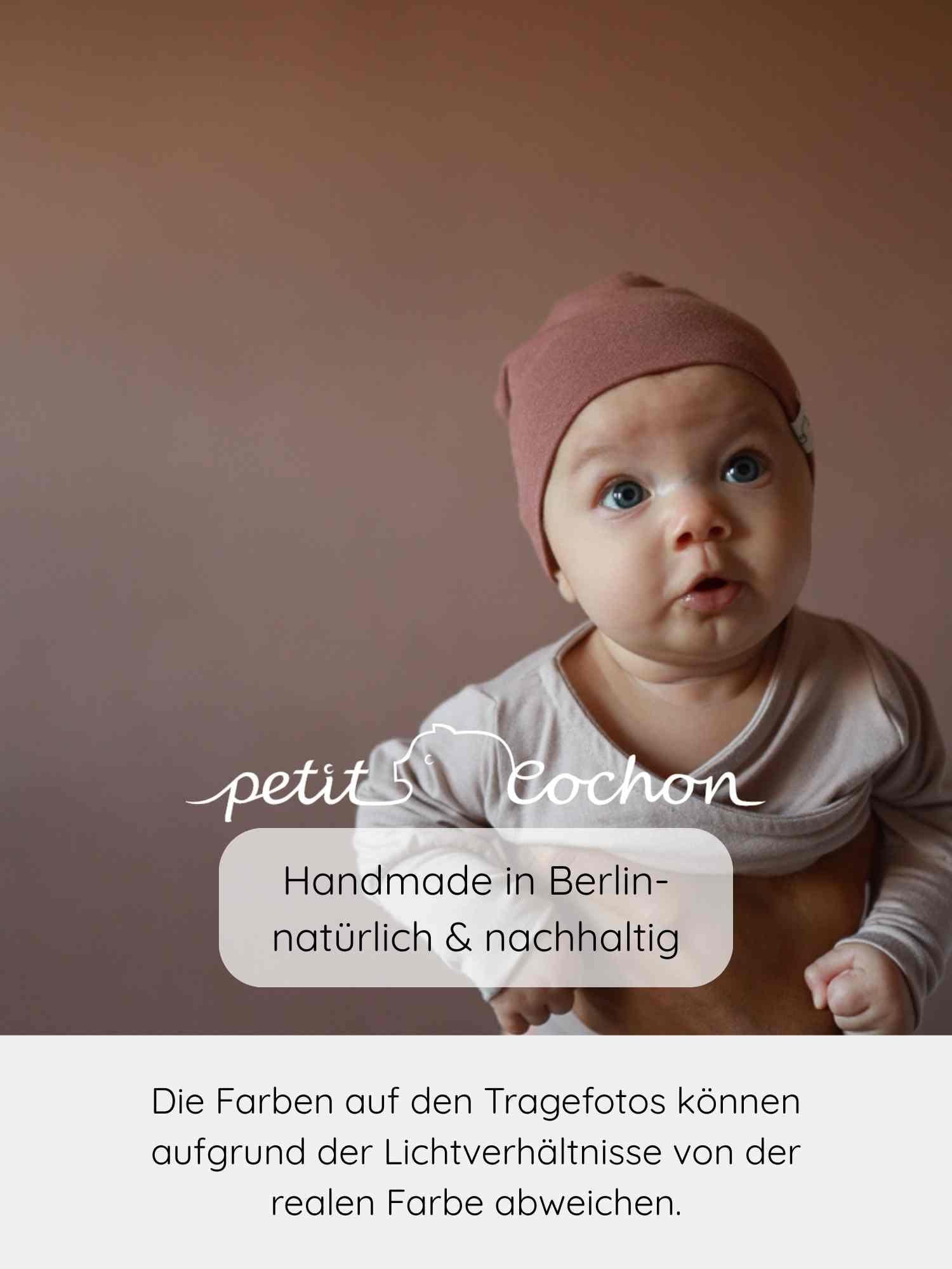 Ein Baby trägt den Loopbody Bambusviskose - Cremepuder von petit cochon, mitwachsender, hautfreundlicher und bequemer Babybody aus atmungsaktivem, antibakteriellem Bambusstoff, der das Wickeln erleichtert.