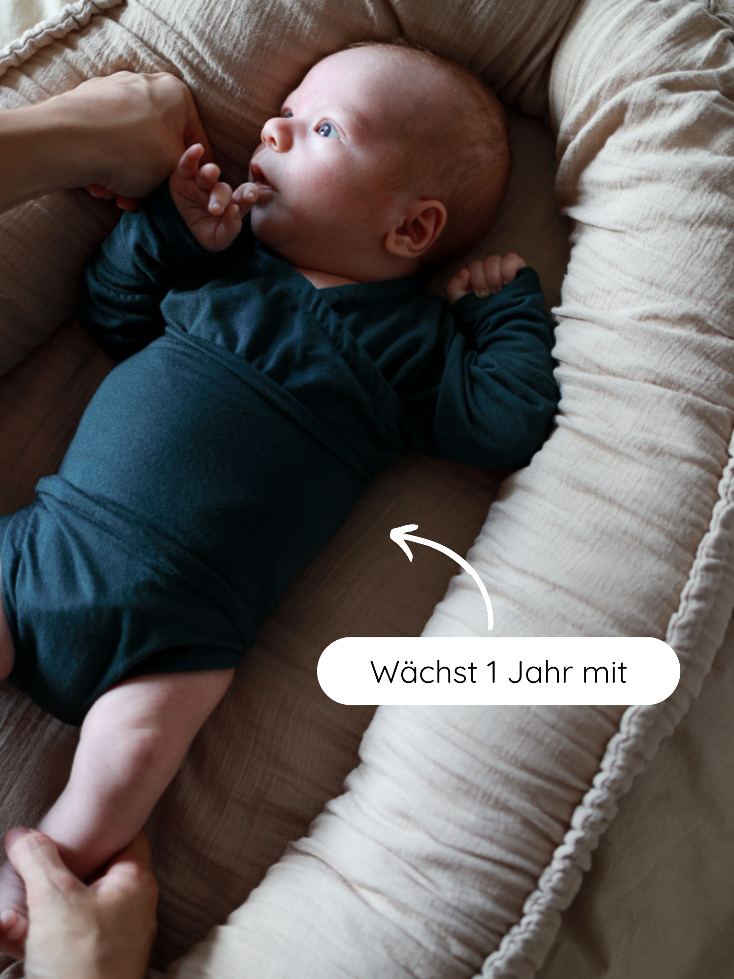 Ein Baby liegt in einem beige-farbenen Nest, getragen von Erwachsenen. Es trägt den Loopbody Bambusviskose in Nachtblau, der über 1 Jahr mitwächst und Komfort bietet.