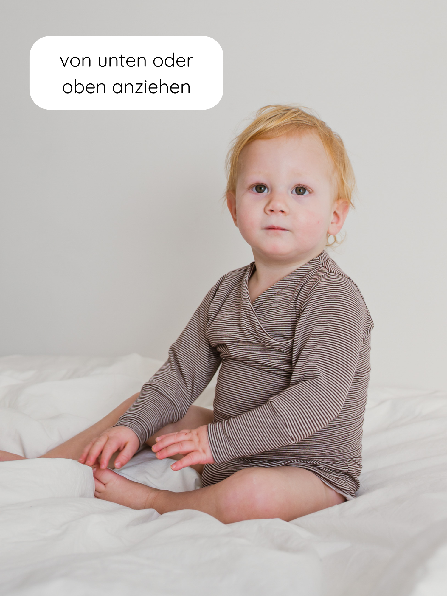 Ein Kleinkind trägt einen Loopbody Bio-Baumwolle-Ringel Schoko, einen braun-weiß gestreiften, mitwachsenden Babybody. Eine Sprechblase erklärt das einfache Anziehen des Bodys von oben oder unten.