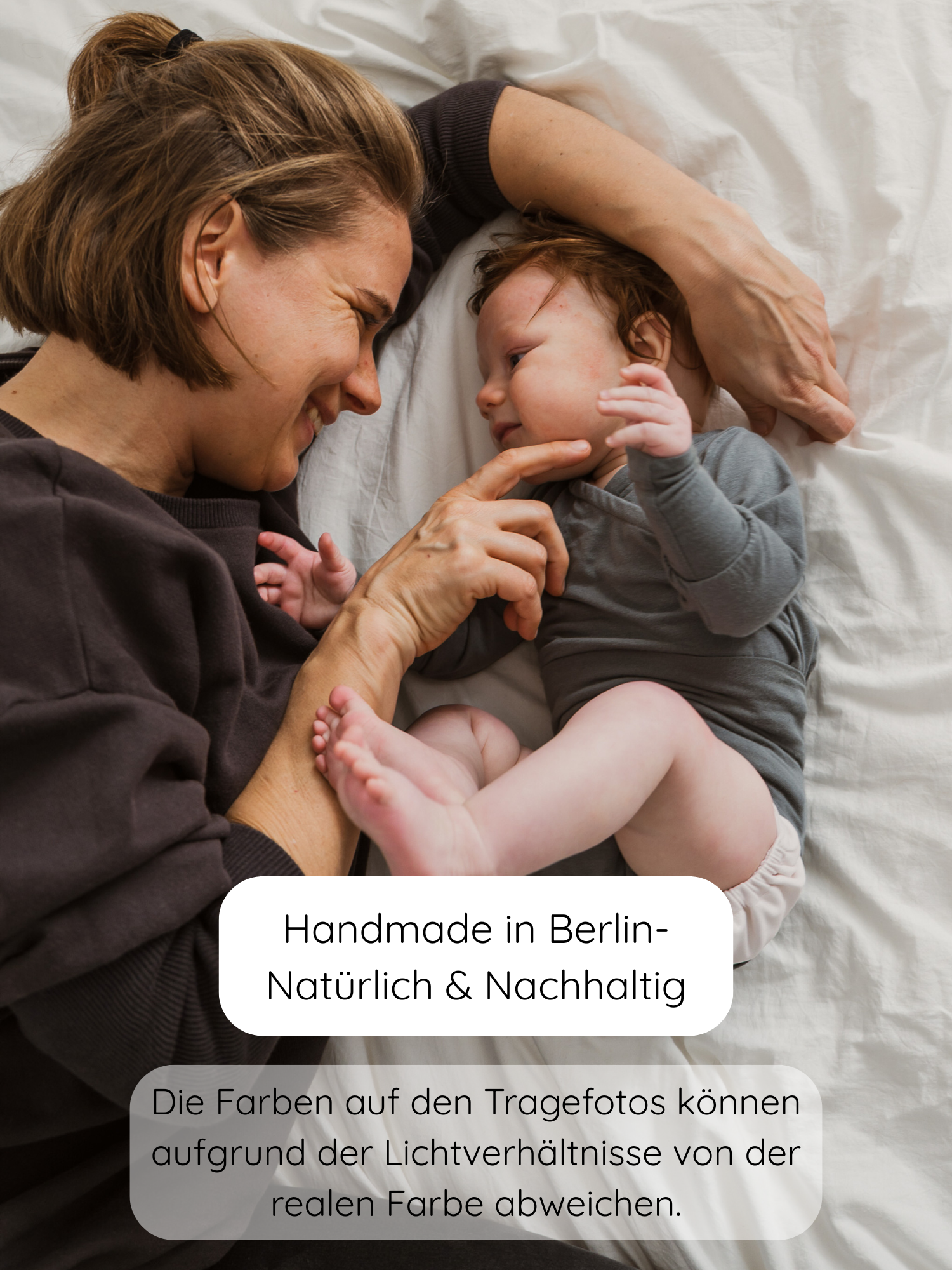 Mutter und Baby lächeln auf dem Bett. Das Baby trägt den Loopbody Kaschmir-Mix in Taube, einen langärmligen, weichen und mitwachsenden Body aus Kaschmir-Mix, handgemacht in Berlin.