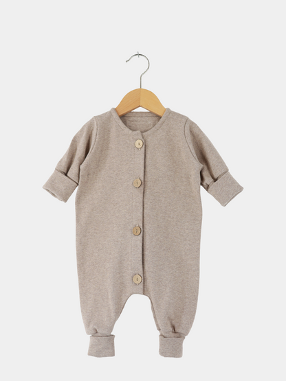 Mini Overall Feinstrick - Hafer Meliert, langärmeliger Baby-Strampler aus weichem, meliertem Feinstrick-Jersey mit Holzknöpfen und umschlagbaren Bündchen an Ärmeln und Beinen, auf einem Holzkleiderbügel hängend.