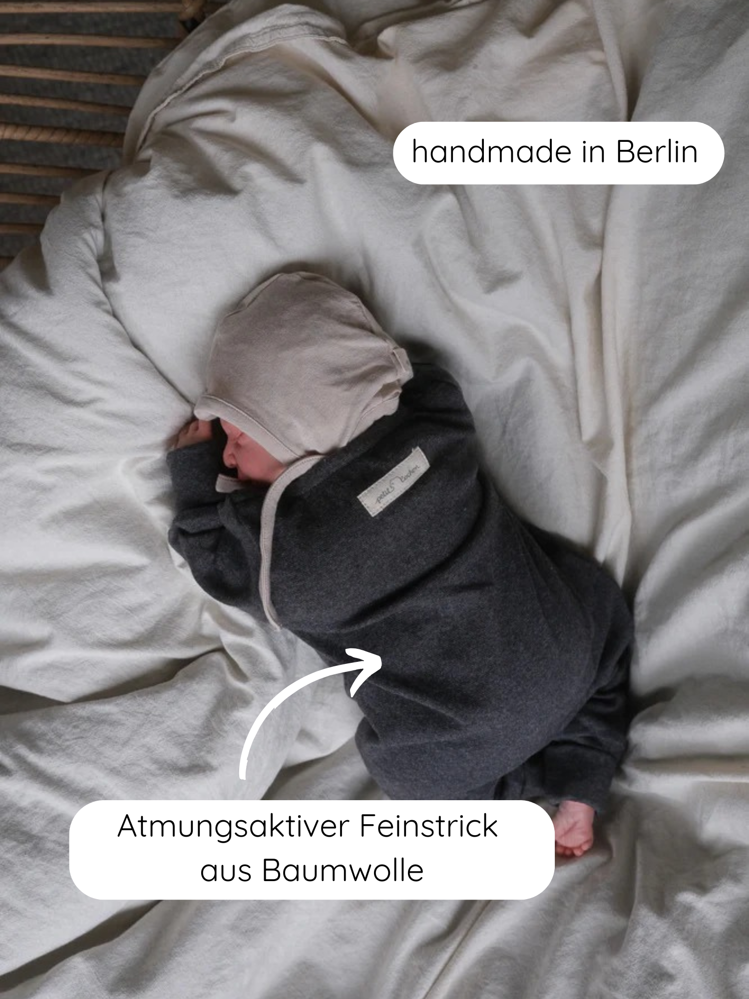 Neugeborenes schläft auf weicher Bettwäsche, trägt Mini Overall Feinstrick - Ruß Meliert, dunkle Farbe, mit hellbeiger Mütze. Call-outs: handmade in Berlin, Atmungsaktiver Feinstrick aus Baumwolle.