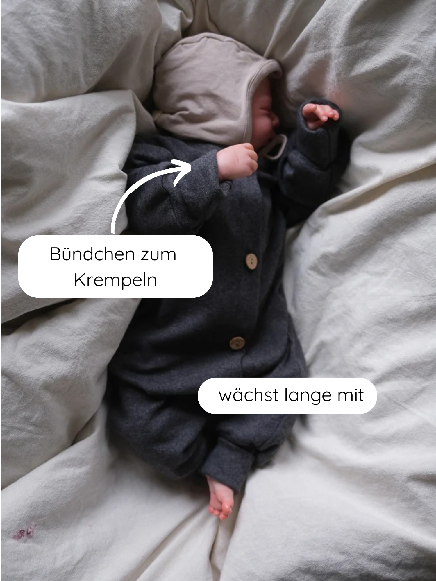 Neugeborenes in einem Mini Overall Feinstrick - Ruß Meliert aus weichem Feinstrick-Jersey mit Kapuze und Holzknöpfen, liegend auf einer hellen Decke. Bündchen zum Krempeln, wächst lange mit.