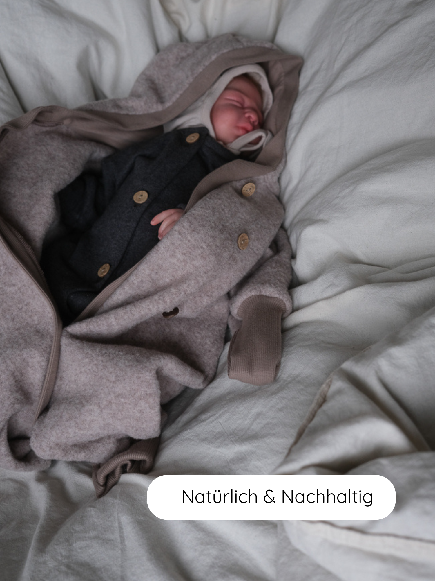 Neugeborenes schläft in einem Mini Overall Feinstrick - Ruß Meliert, mit Holzknöpfen und Kapuze. Der Overall ist aus weichem, meliertem Feinstrick-Jersey, unterlegt mit Natürlich & Nachhaltig.
