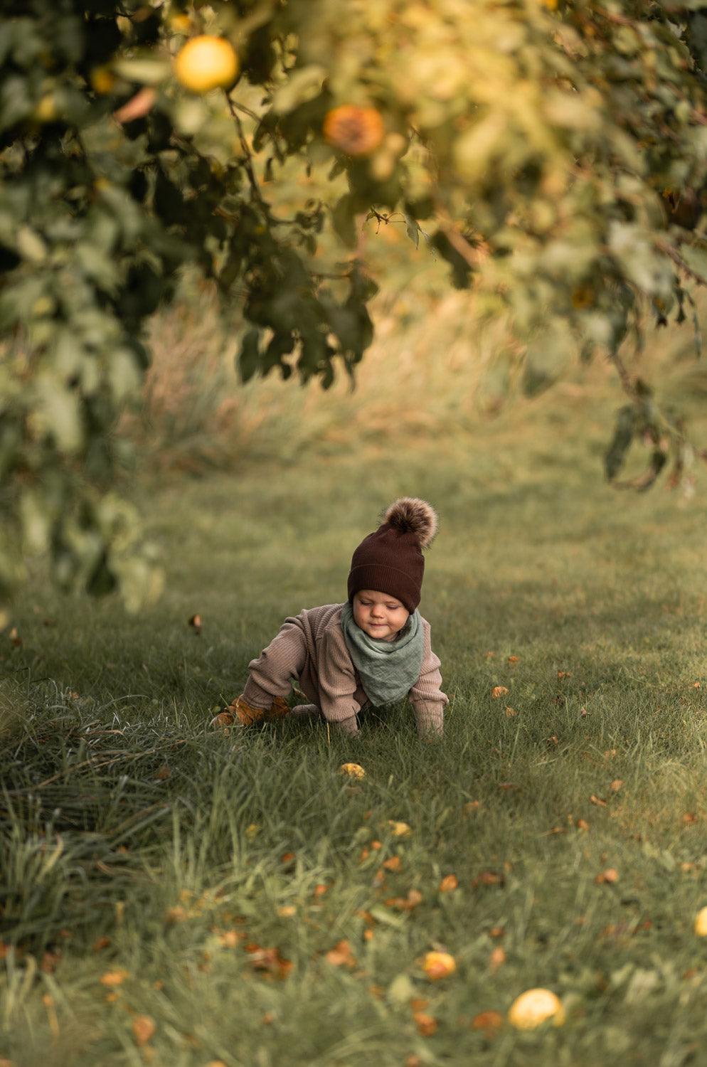 Baby im Mini Overall Rippstrick - Hafer, krabbelt auf Gras im Freien. Der Overall aus recycelter Baumwolle bietet Komfort und wächst mit. Perfekt für das ganze Jahr.