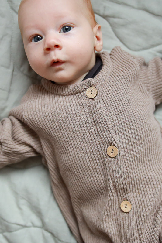 Baby liegt auf einer Decke, trägt den Mini Overall Rippstrick - Hafer ein Strampler für Babys aus recycelter Baumwolle, bequemer Schnitt mit Krempelbündchen für Wachstum.