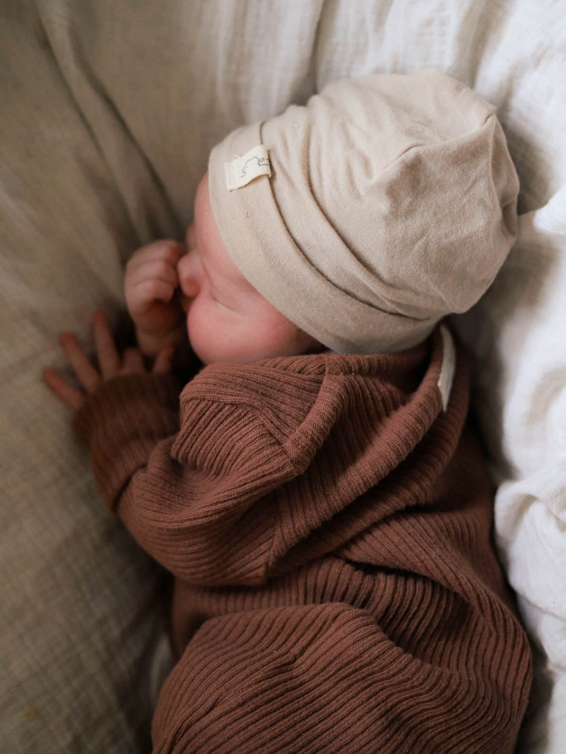 Baby schläft im Mini Overall Rippstrick - Nougat, gemütlicher Strickanzug aus recycelter Baumwolle, perfekt für Komfort und Wärme, mit Beanie.