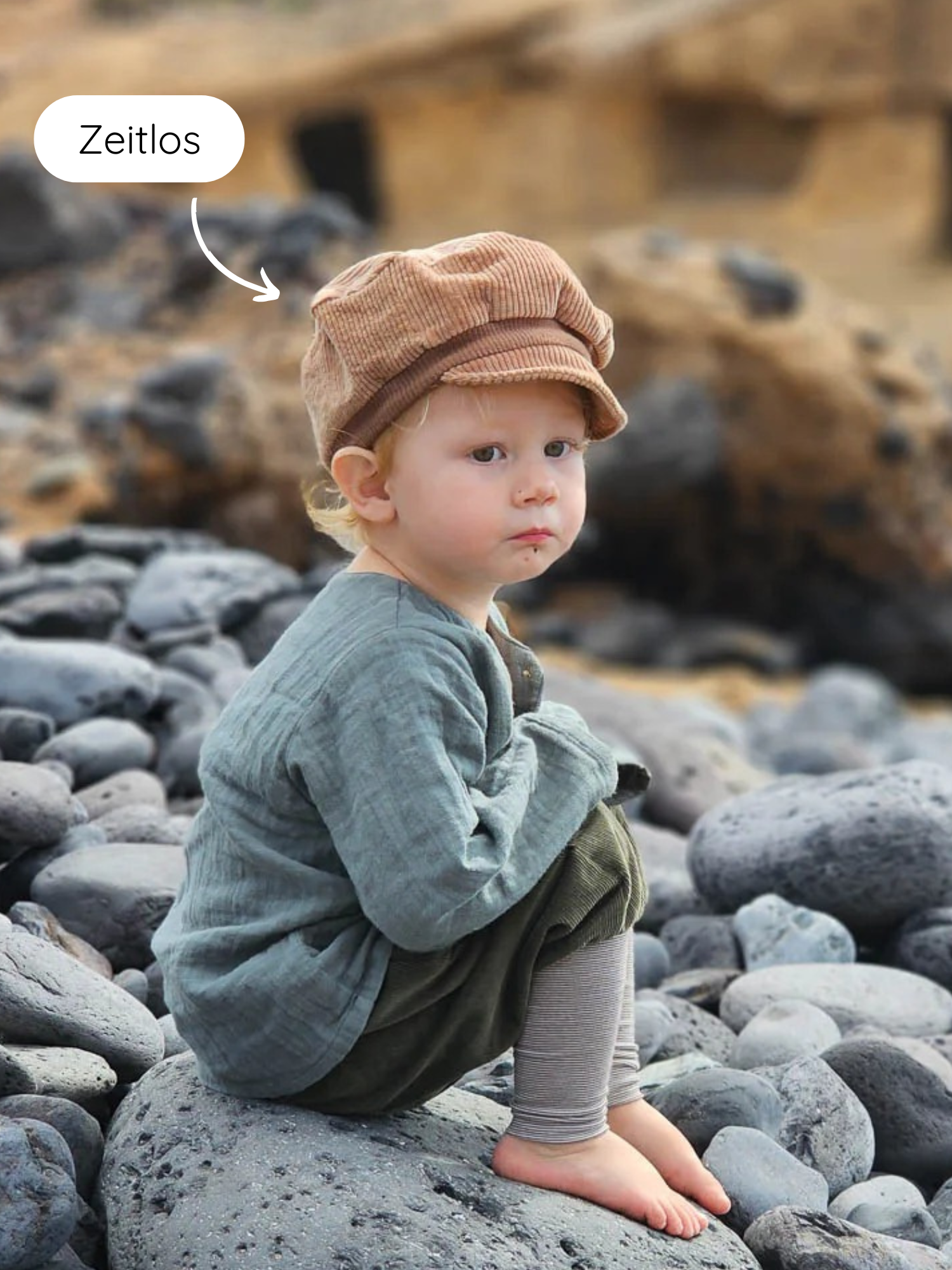 Ein Kleinkind trägt die Michelmütze Breitcord Stretch - Weizen, eine weiche, handgemachte Cord-Kappe mit kleinem Schirm und verstellbarem Band, ideal für kühle Tage und robuste Abenteuer.