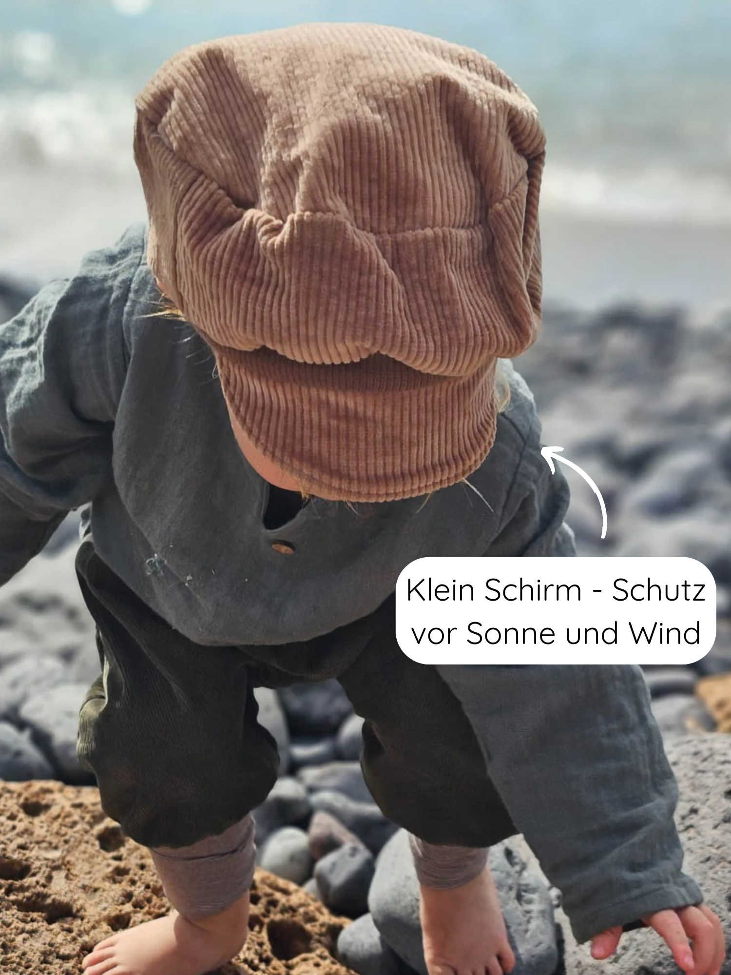 Kleinkind am Strand trägt Michelmütze Breitcord Stretch - Weizen: Eine weiche, formstabile Kappe mit kleinem Schirm, ideal für Übergangstage, schützt vor Sonne und Wind, handgefertigt in Berlin.