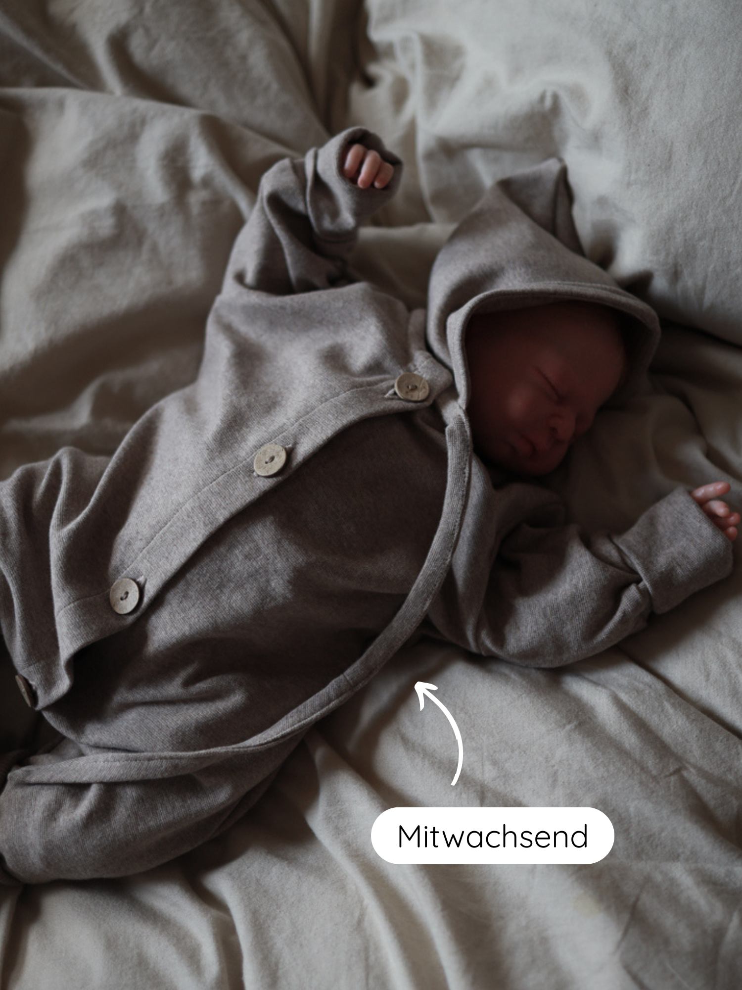 Ein schlafendes Neugeborenes trägt einen Mini Overall Feinstrick - Hafer Meliert, einen neutral-grauen, knöpfbaren, kapuzenartigen Strampler, der mit dem Kind wächst. Weiche, elastische Baumwollqualität, ideal für empfindliche Haut.