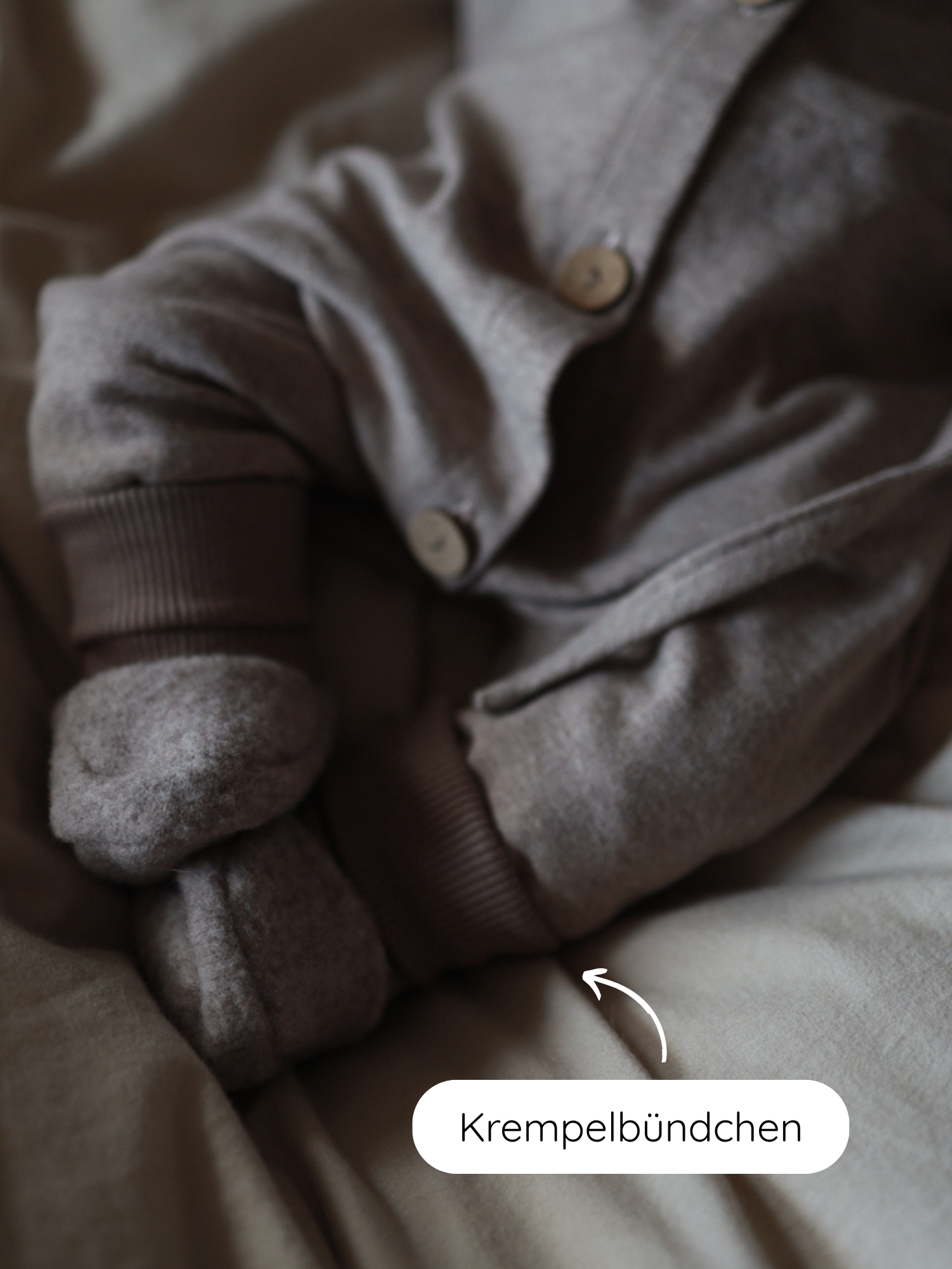 Mini Overall Feinstrick - Hafer Meliert: Nahaufnahme eines weichen, braunen Babyoutfits mit Holzknöpfen und Krempelbündchen, ideal zum Schlafen oder Spielen, aus meliertem Feinstrick-Jersey, komfortabel und nachhaltig gefertigt.