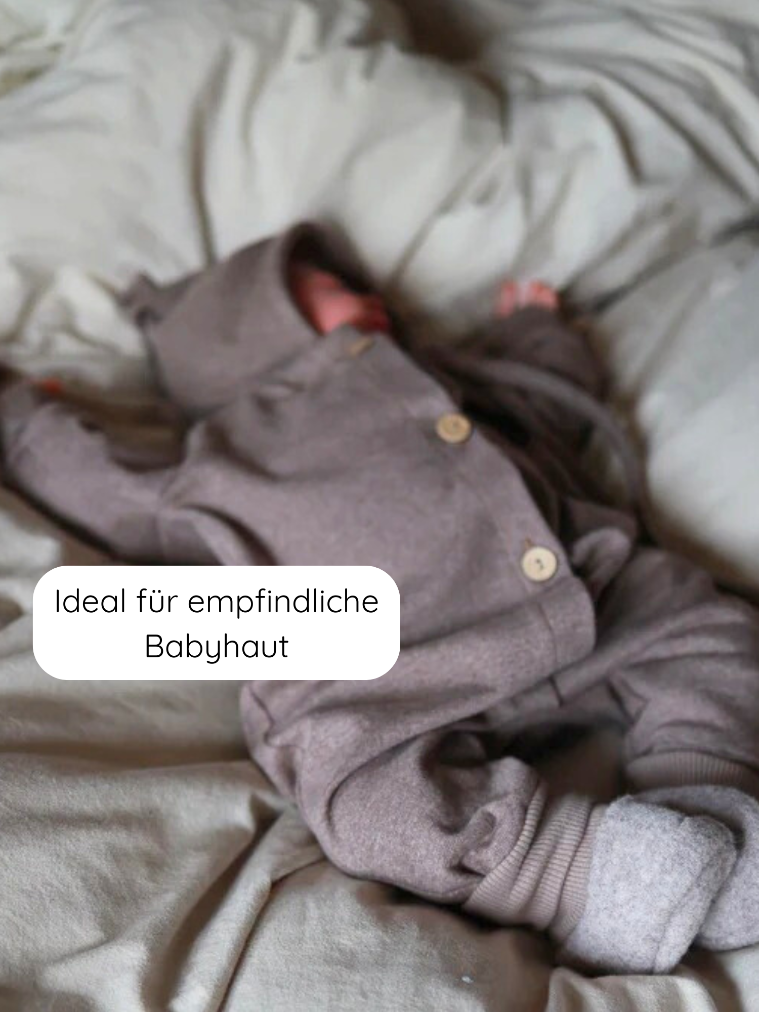 Baby in einem Mini Overall Feinstrick - Praline Meliert, bestehend aus einer Kapuzenjacke mit Holzknöpfen und passenden Hosen mit umgeschlagenen Bündchen, auf einem weichen Bett liegend. Ideal für empfindliche Babyhaut.