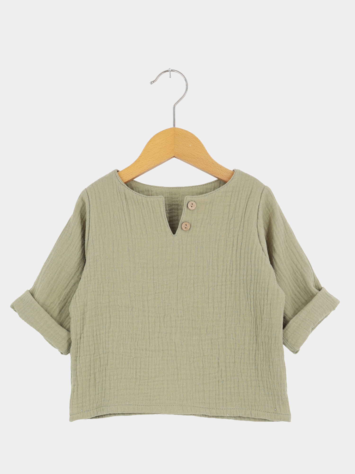 Hemdchen Musselin - Salbei, ein leichtes, langärmeliges Kinderpullover aus weichem, texturiertem Musselin. Mit V-Ausschnitt, zwei Holzknöpfen, und hochgekrempelten Ärmeln, ideal für warme Tage.
