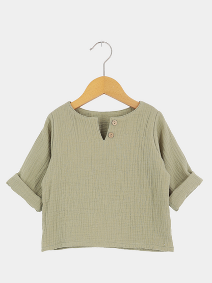 Hemdchen Musselin - Salbei, ein leichtes, langärmeliges Kinderpullover aus weichem, texturiertem Musselin. Mit V-Ausschnitt, zwei Holzknöpfen, und hochgekrempelten Ärmeln, ideal für warme Tage.