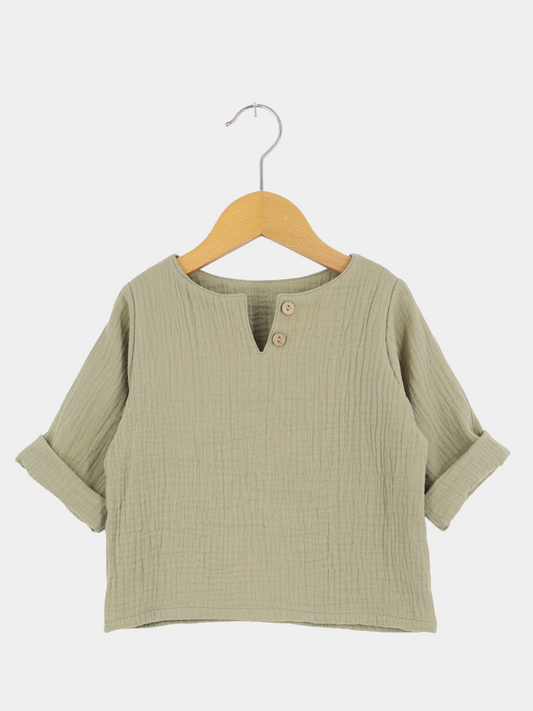Hemdchen Musselin - Salbei, ein leichtes, langärmeliges Kinderpullover aus weichem, texturiertem Musselin. Mit V-Ausschnitt, zwei Holzknöpfen, und hochgekrempelten Ärmeln, ideal für warme Tage.