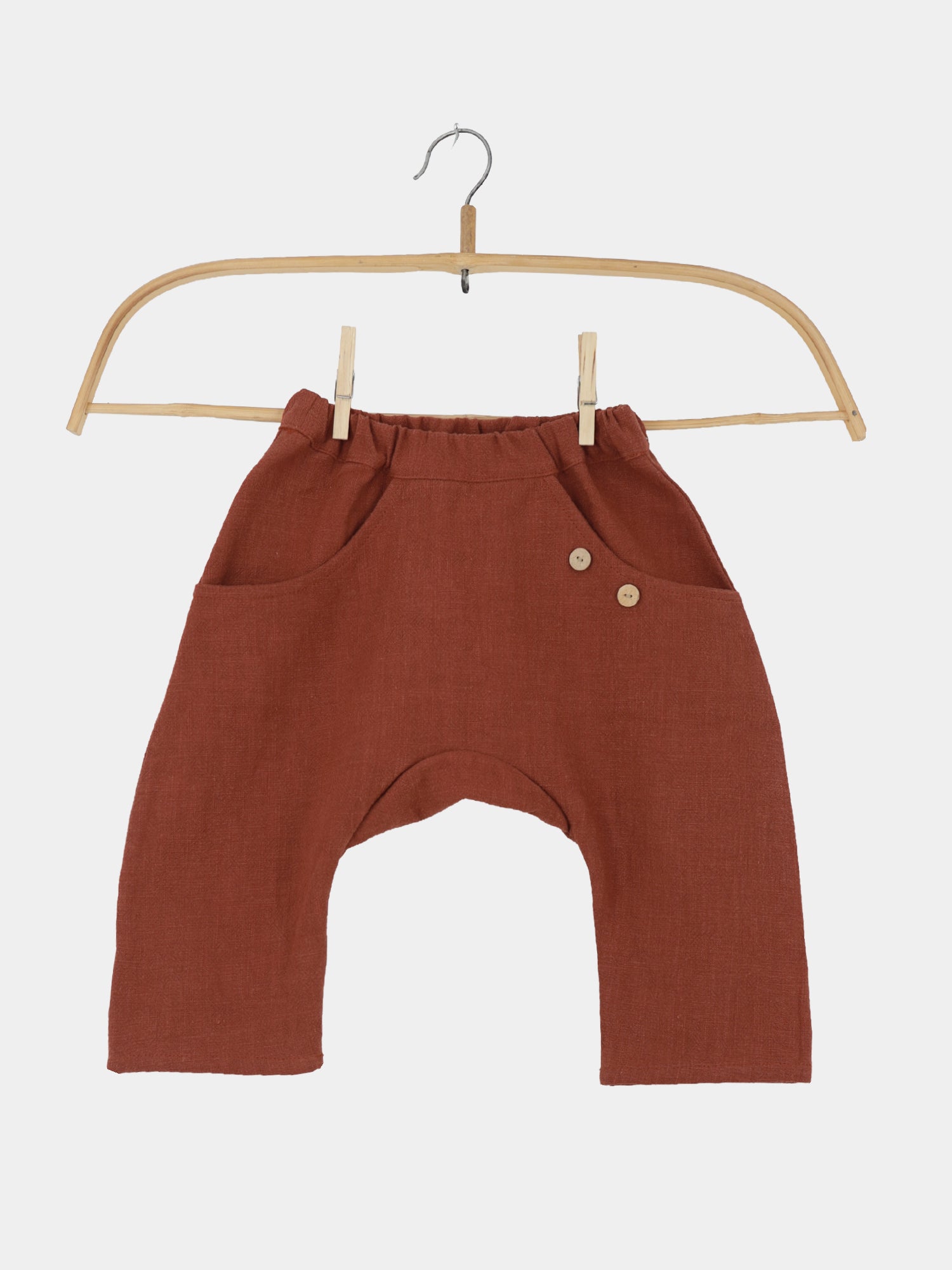 Sommerknicker Leinen - Ziegel: Kinderharemshose aus leinenartigem Stoff mit elastischem Bund, zwei Fronttaschen, kleinen Holzknöpfen, an Holzbügel befestigt, ideal für Bewegungsfreiheit und Komfort.