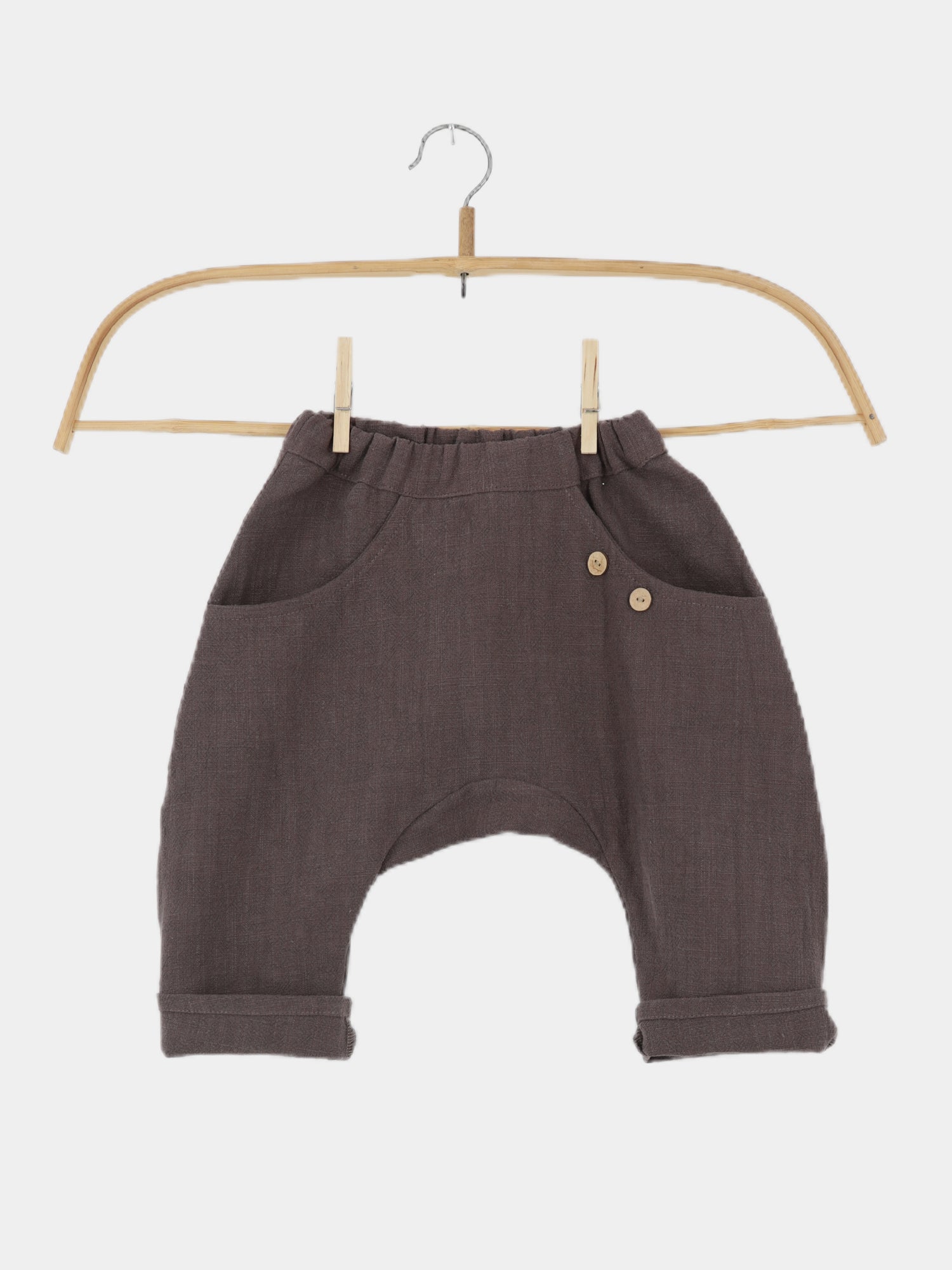 Sommerknicker Leinen - Erde: Locker geschnittene, dunkle graubraune Kleinkindhose mit elastischem Bund, umgeschlagenen Bündchen und kleinen Holzknopf-Details, auf einem Holzbügel vor weißem Hintergrund präsentiert.