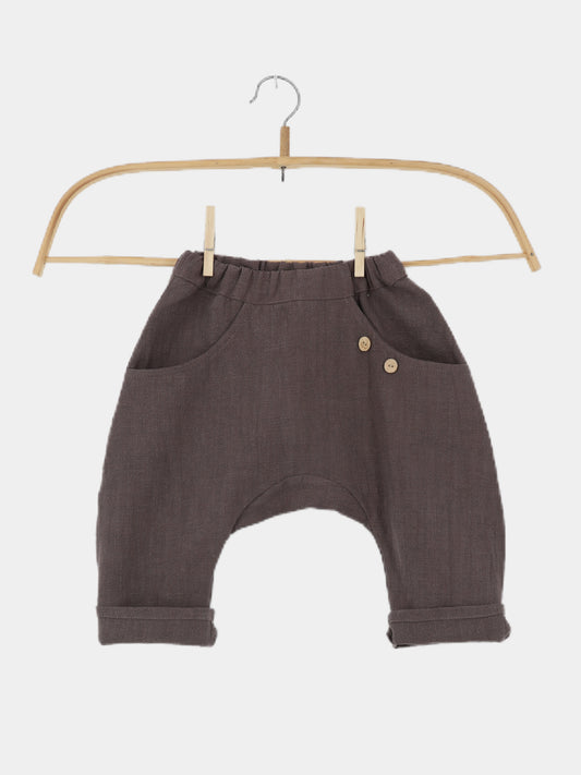 Sommerknicker Leinen - Erde: Locker geschnittene, dunkle graubraune Kleinkindhose mit elastischem Bund, umgeschlagenen Bündchen und kleinen Holzknopf-Details, auf einem Holzbügel vor weißem Hintergrund präsentiert.