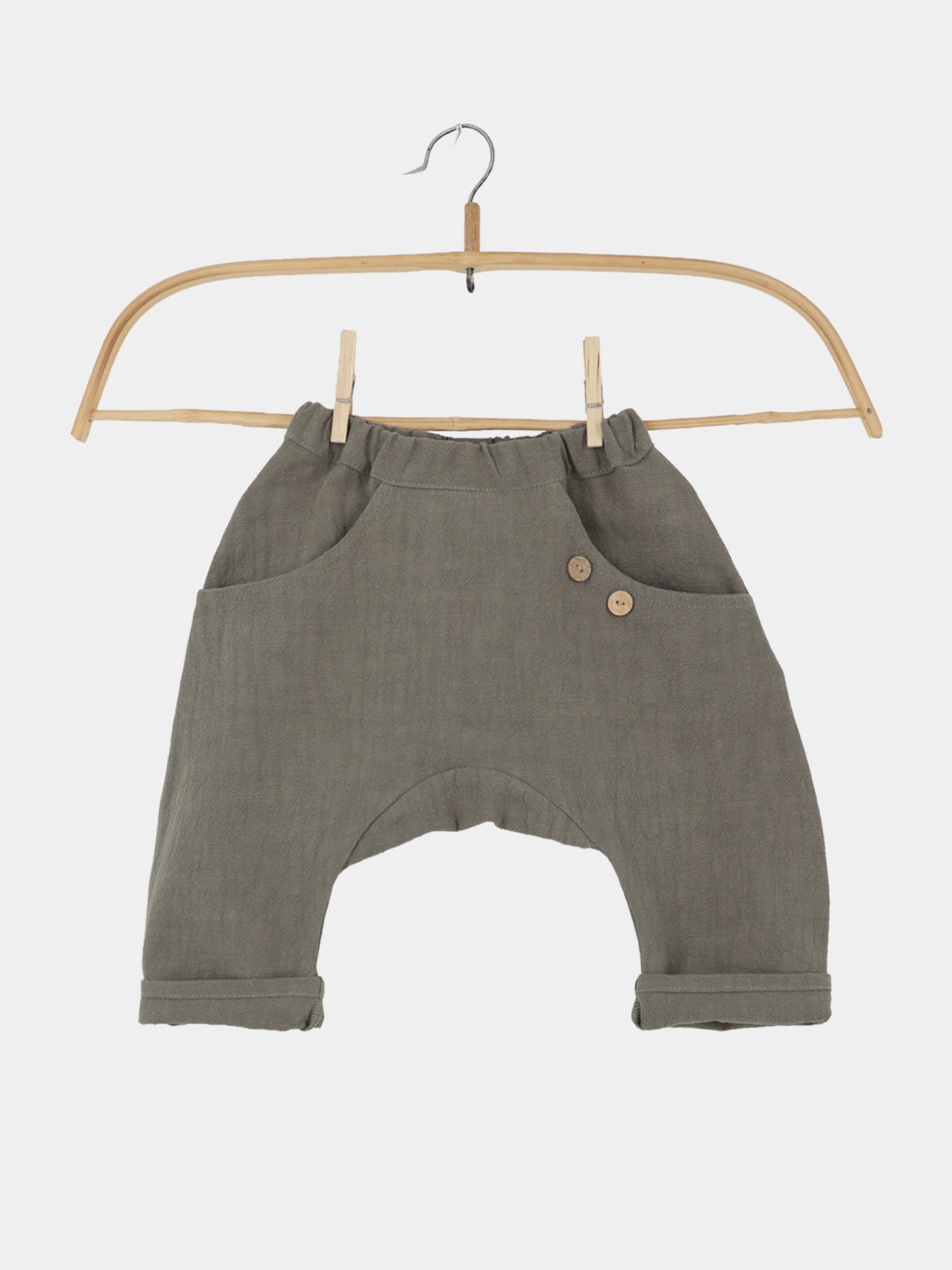 Sommerknicker Leinen - Oliv: Olive-grüne Haremshose für Babys mit leichtem Gummibund, zwei Seitentaschen, dekorativen Holzknöpfen, gerollten Bündchen an den Knöcheln, aus atmungsaktivem, strapazierfähigem Leinenstoff, hängend an einem Holzbügel.