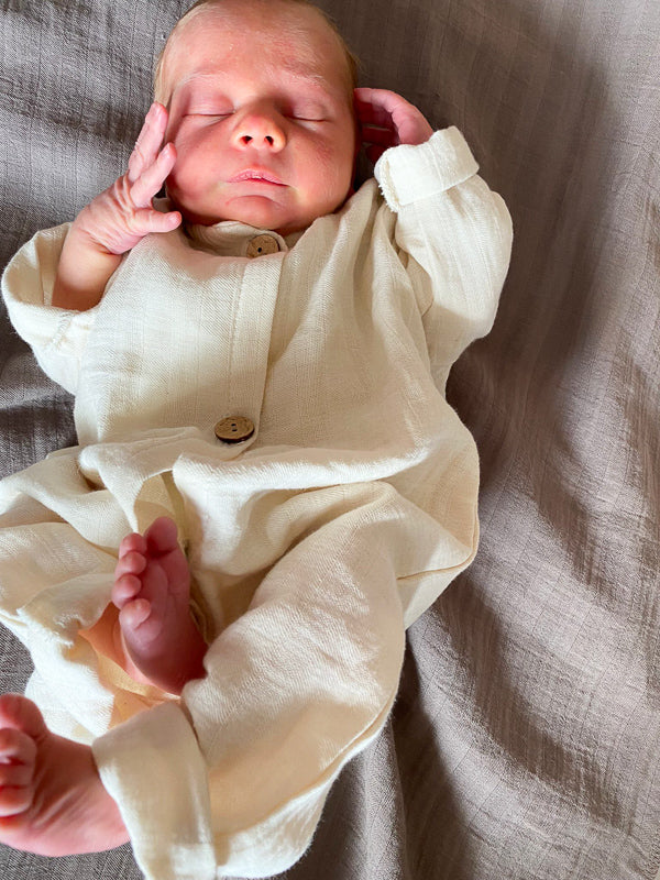 Baby schläft auf einer Decke, trägt den Mini Overall Bio-Musselin - Natur, welcher bequem ist und sich an das Wachstum des Kindes anpasst. Strampler und Erstausstattung Baby
