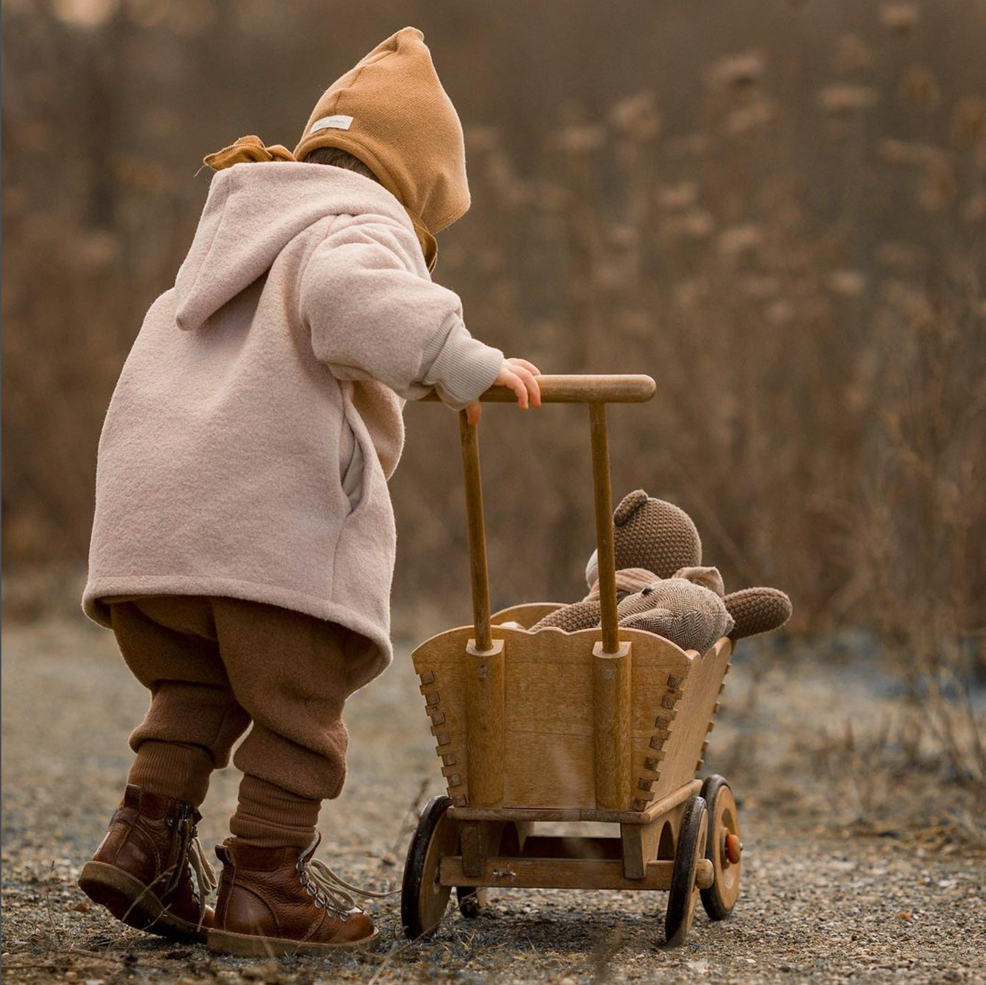 Kind schiebt Bollerwagen. Trägt Wichteljacke Wollwalk Sand und Knickerbocker Wollwalk Nougat. Winterkleidung für Kinder aus Berlin.