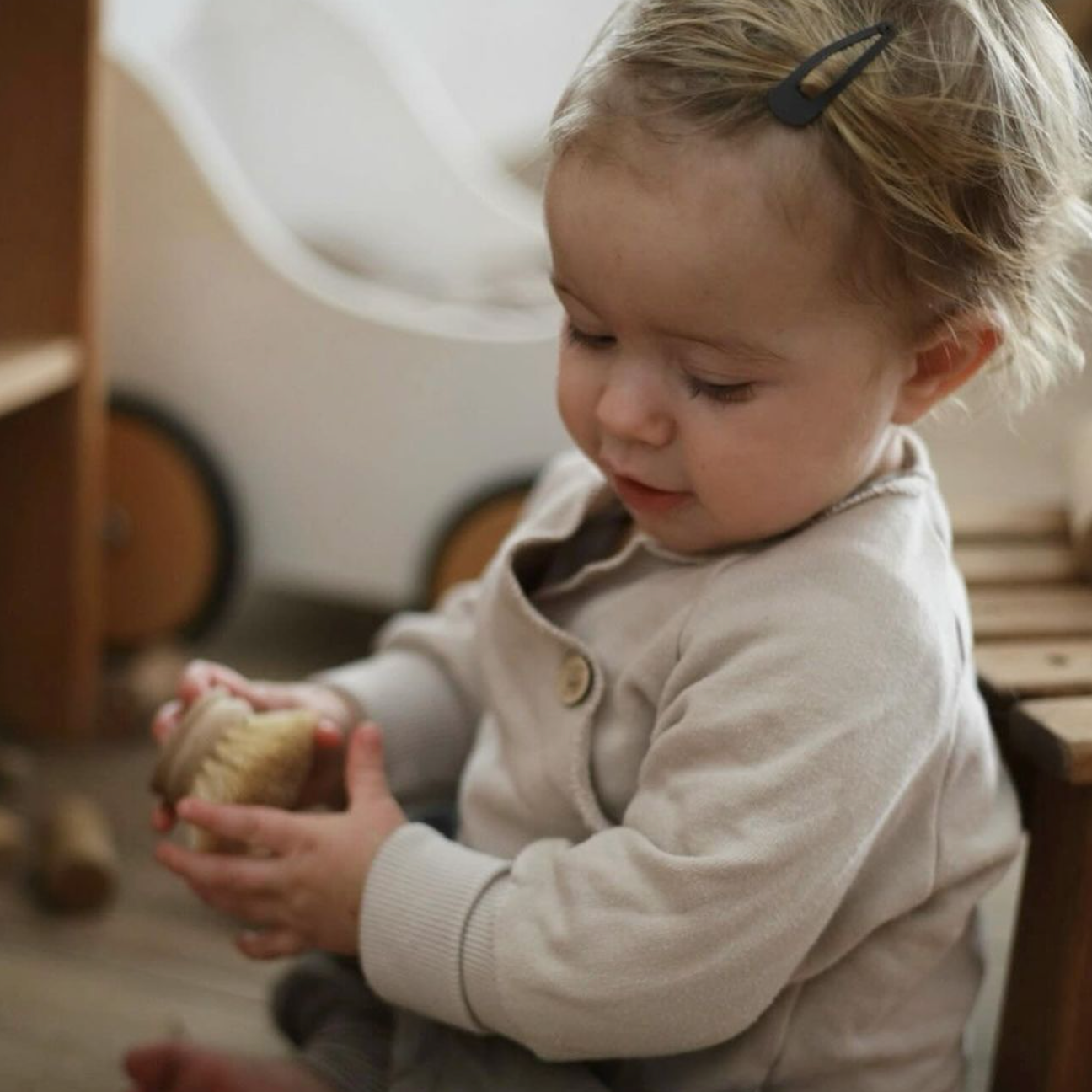 Kind spielt mit Bürste. Trägt Schlüttli Bio-Baumwolle Sand, super bequeme und nachhaltige Kinderkleidung aus Deutschland.