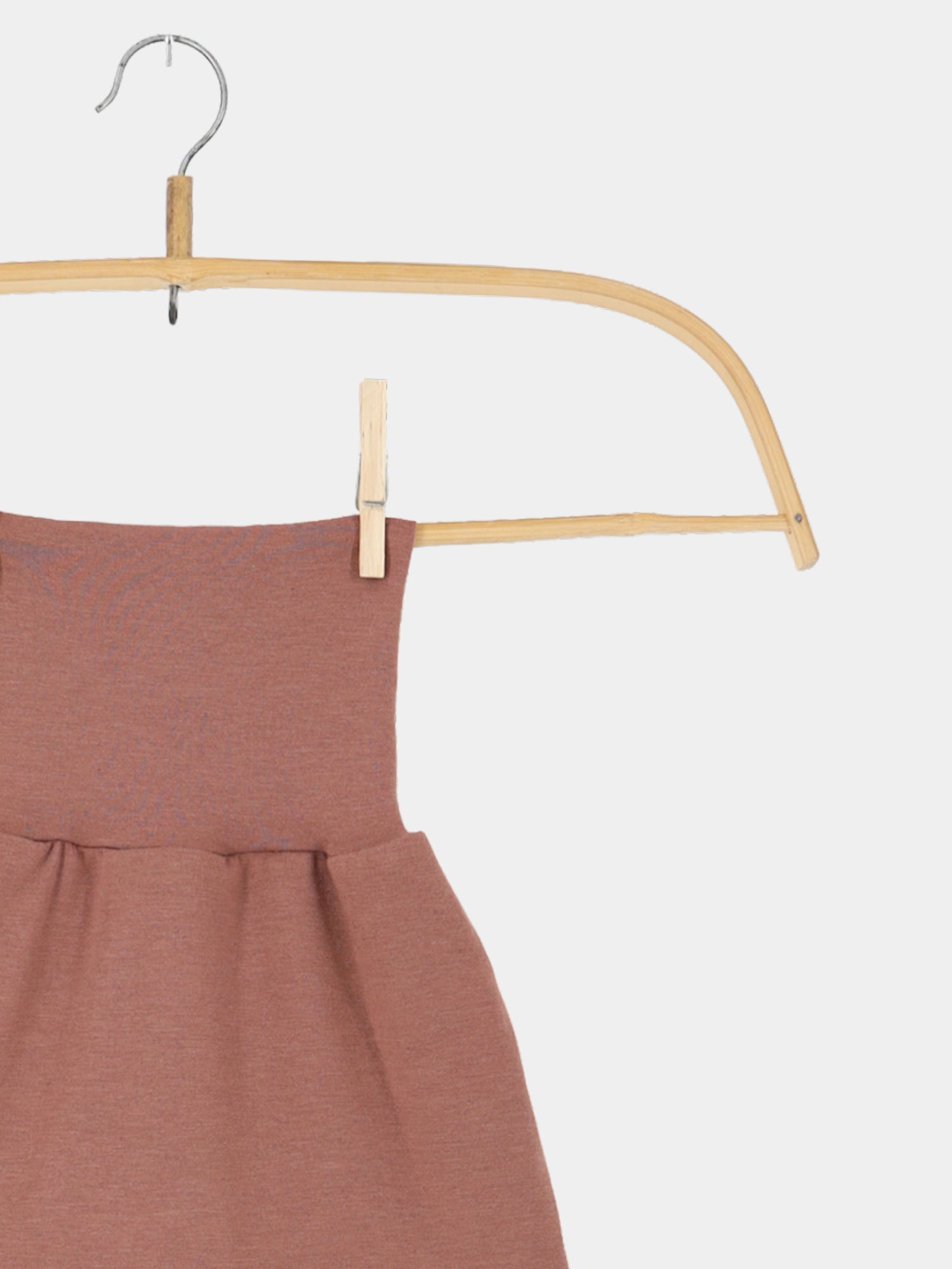 Baby Strampel- und Pucksack Kaschmir-Mix - Zimt aus Holzkleiderbügel mit Metallhaken, gesichert durch Holzwäscheklammer. Ideal für Neugeborene, bietet Geborgenheit und Komfort in zeitloser Sandfarbe.