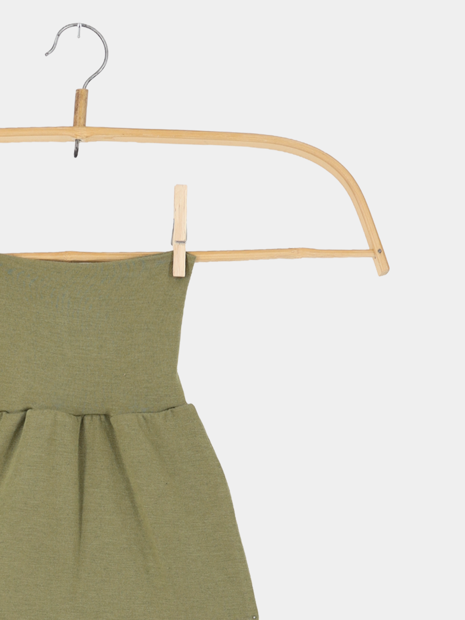 Baby Strampel- und Pucksack Kaschmir-Mix - Pistazie, ein olivgrünes Baby-Kleidungsstück auf einem hellen Holzkleiderbügel mit Metallhaken, fixiert durch einen kleinen Holz-Wäscheklammer.