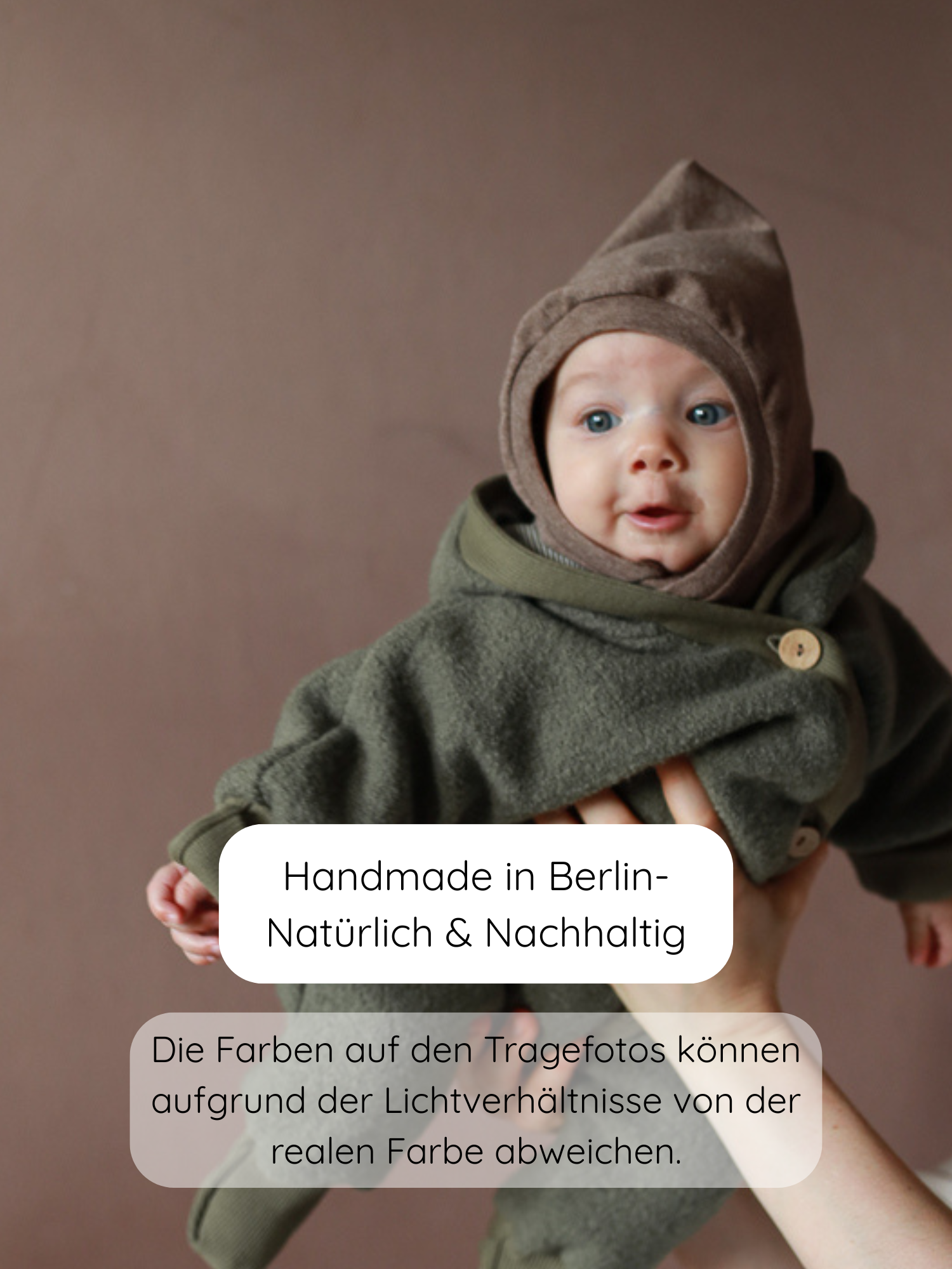 Ein Baby trägt eine Schlupfmütze Feinstrick-Jersey - Praline Meliert, gehalten von Erwachsenen vor einem warmen Hintergrund. Die Mütze ist leicht, atmungsaktiv, ideal für Übergangszeiten und windige Tage.