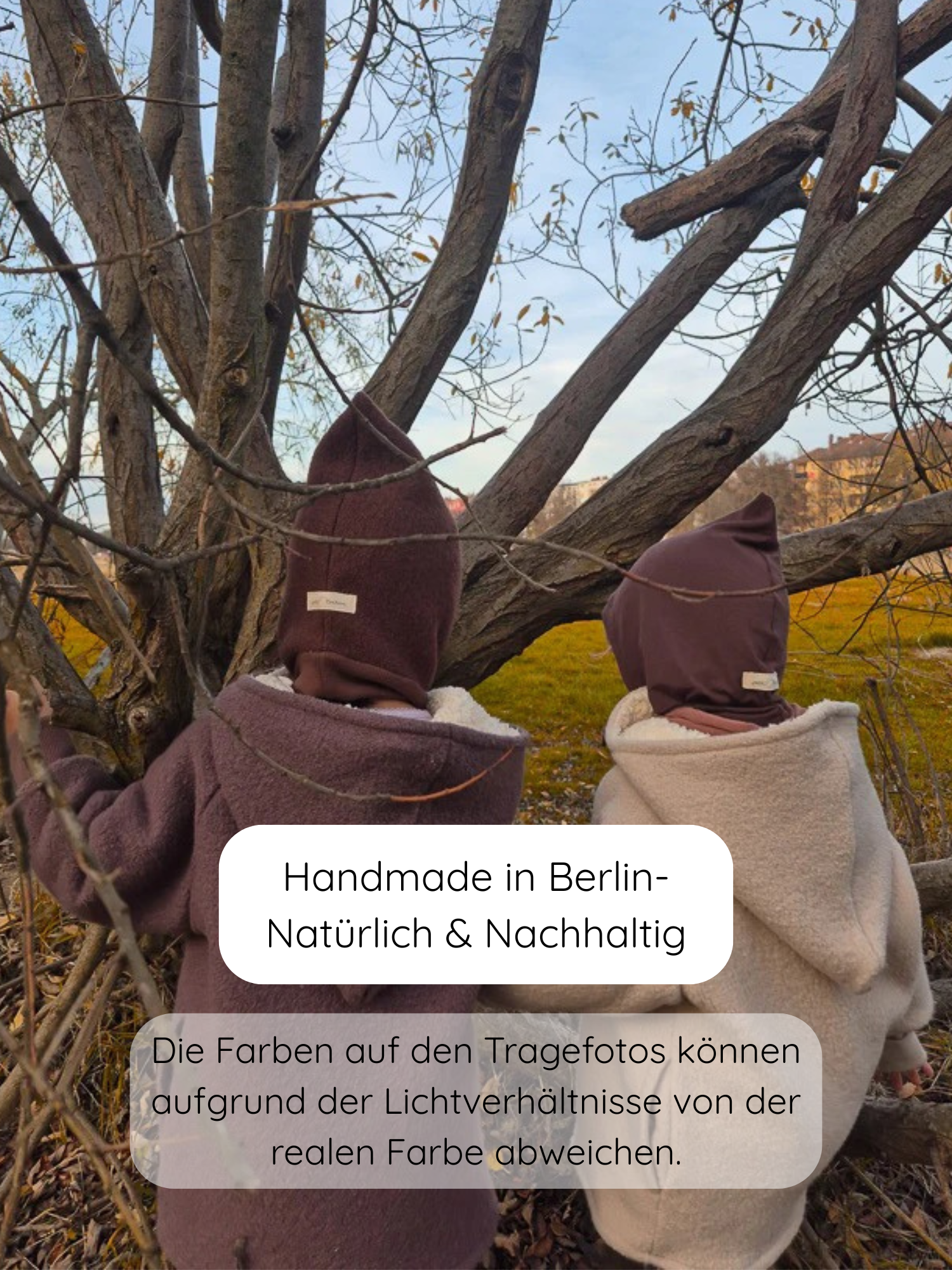 Zwei Kinder tragen die Schlupfmütze Wollwalk - Schoko mit passenden Balaclava-Hüten, lehnen an einem Baum im herbstlichen Park. Die Mütze bietet umfassenden Schutz von Kopf bis Hals.