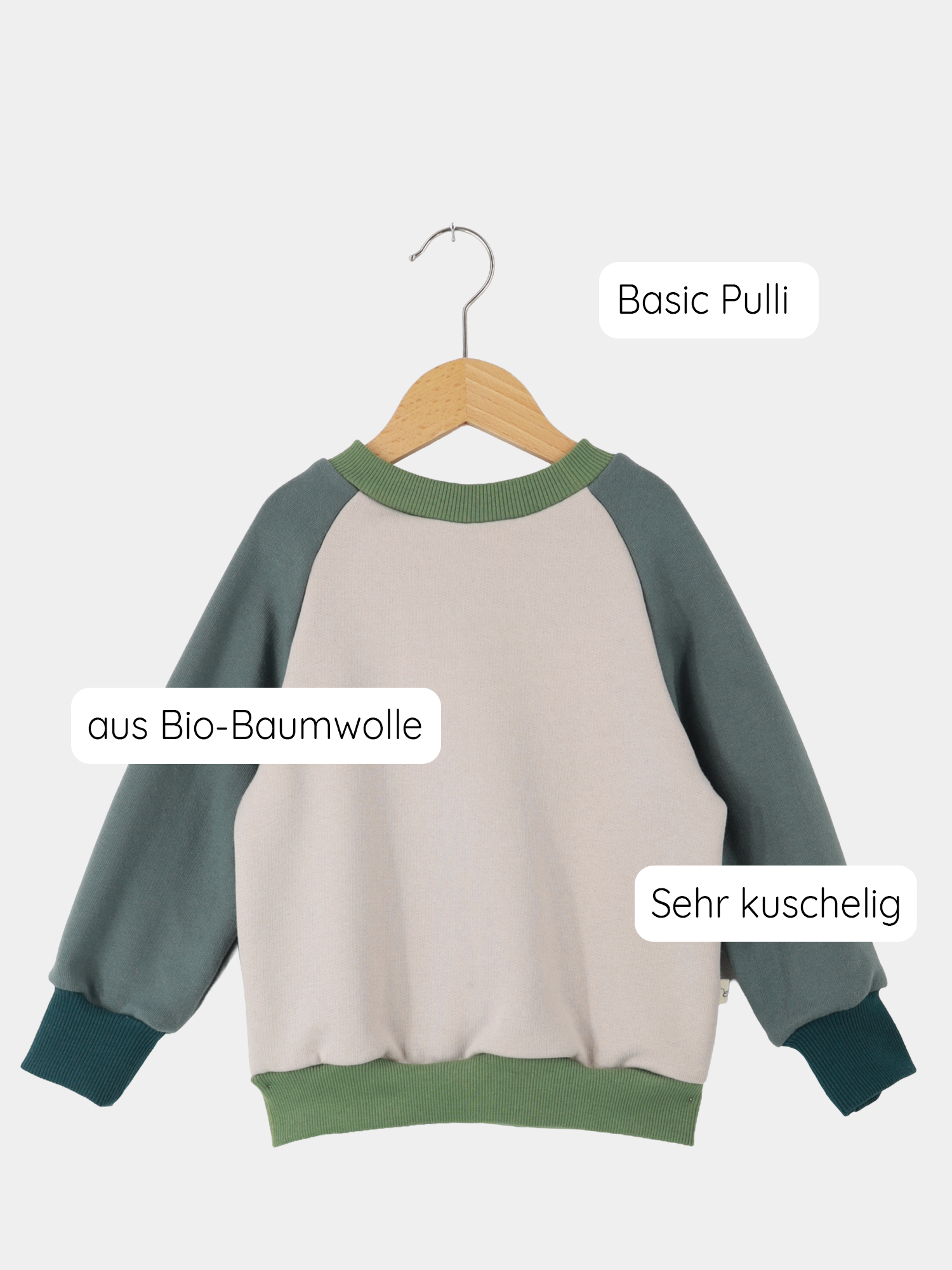 Upcycling-Pulli Bio-Sweat - Drachenwiese: Kinderpullover aus kuscheliger Bio-Baumwolle, zweifarbig mit Raglan-Ärmeln, nachhaltig aus Stoffresten gefertigt, präsentiert auf hölzernem Bügel vor schlichtem Hintergrund.