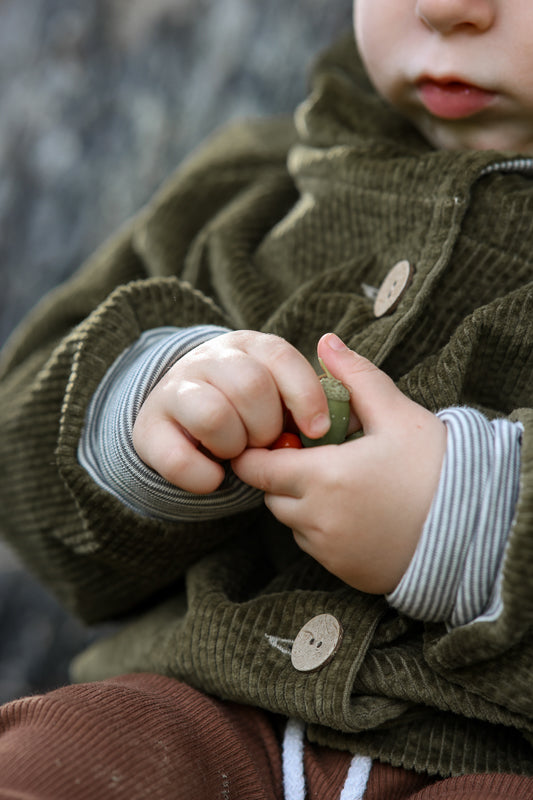 Ein Kind hält die Wichteljacke Breitcord - Kiwi, eine mitwachsende Übergangsjacke mit Ringel-Armbündchen und Wichtelkapuze, die für hohen Tragekomfort und Langlebigkeit steht.