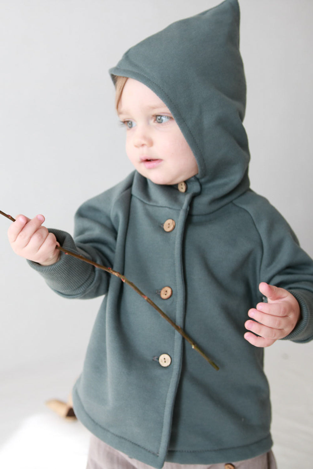 Kind trägt Wichteljacke Bio-Sweat - Taube von PETIT COCHON Berlin, aus 100% Bio-Baumwolle, mit Wichtelkapuze. Perfekt für nachhaltige, langlebige Kinderkleidung.
