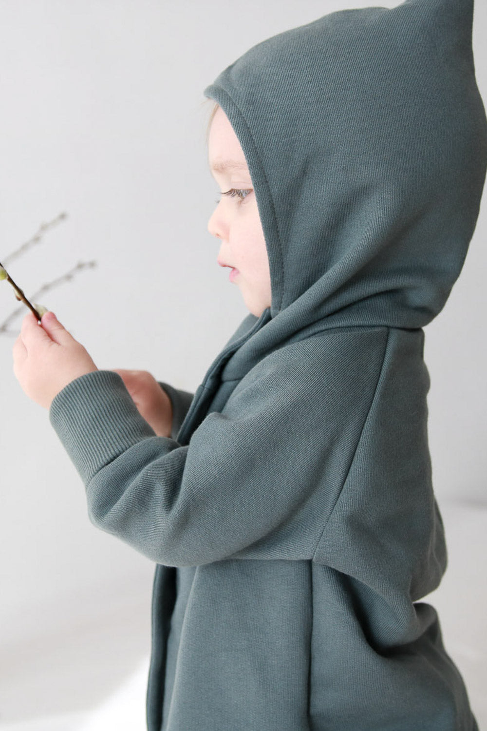 Ein Kind trägt die Wichteljacke Bio-Sweat - Taube von PETIT COCHON Berlin, aus 100% Bio-Baumwolle, mit charakteristischer Kapuze und nachhaltig gefertigt.