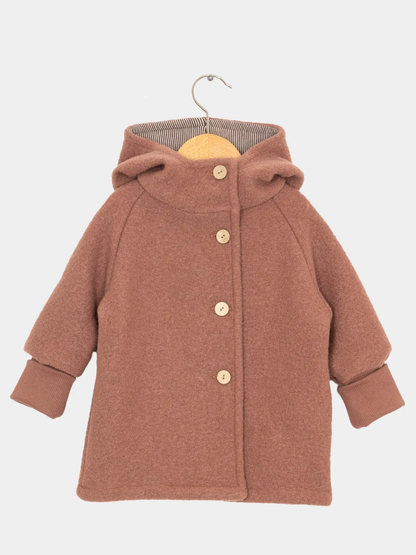 Wichteljacke Wollwalk - Zimt aus weichem Stoff, mit vier Holzknöpfen und geräumiger Kapuze. Lange Ärmel mit dunkelbraunen, krempelbaren Bündchen, präsentiert auf einem Holzkleiderbügel.