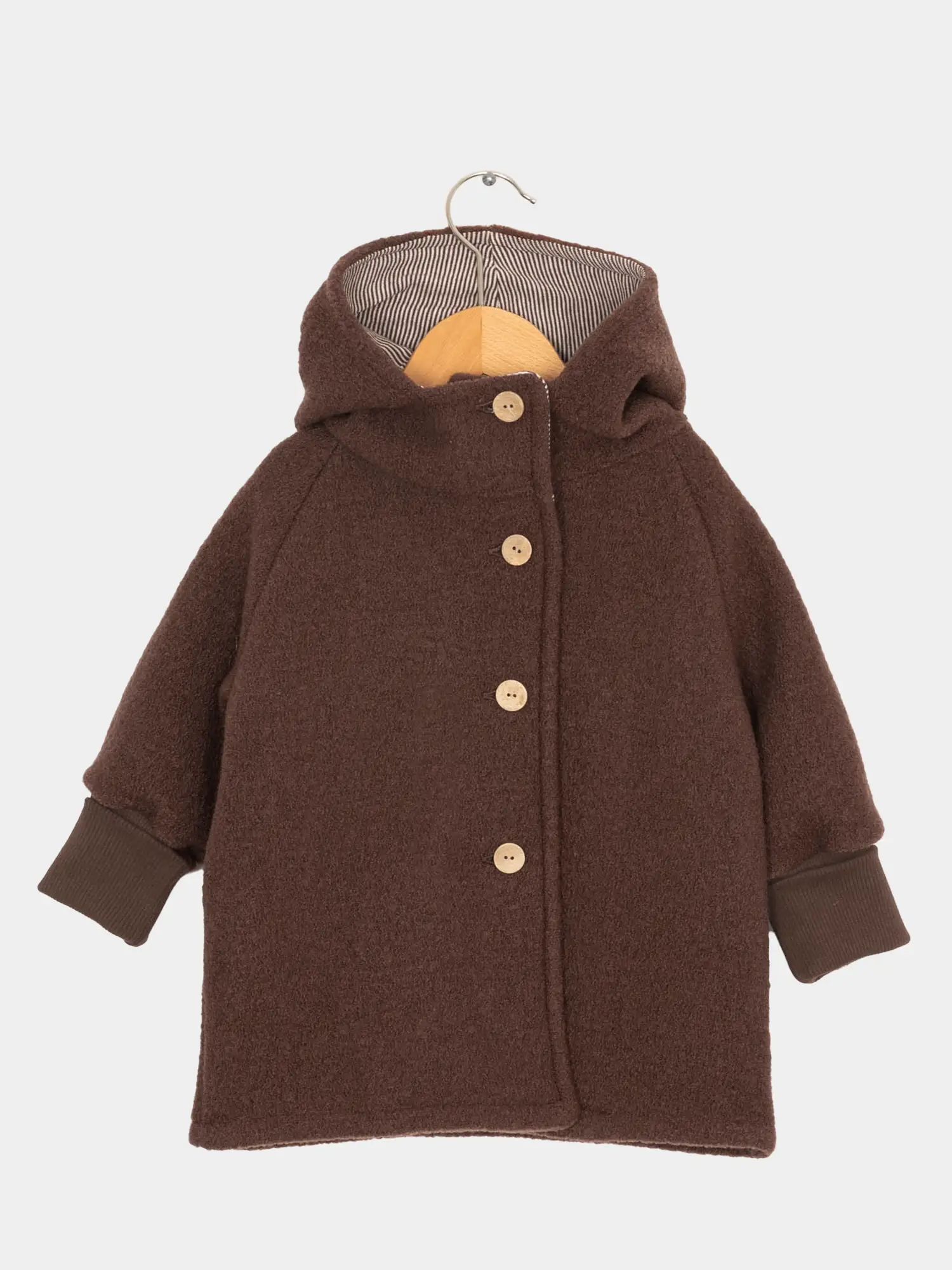 Wichteljacke Wollwalk - Schoko: Kinder-Wintermantel aus strukturiertem Wollstoff mit gestreiftem Kapuzenfutter, langen Raglanärmeln, krempelbaren Bündchen und vier Holzknöpfen, präsentiert auf einem Holzkleiderbügel.