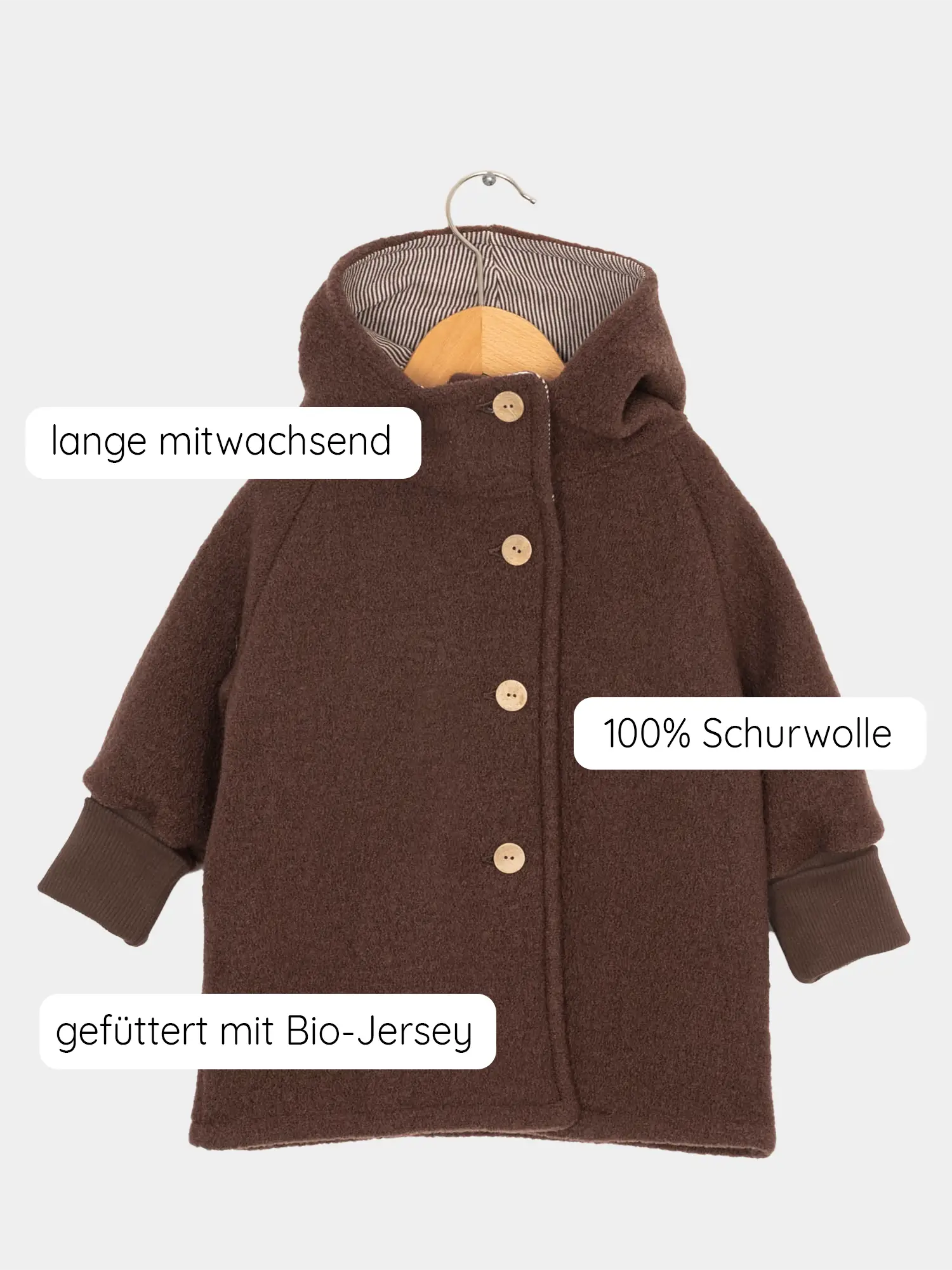 Wichteljacke Wollwalk - Schoko: Kleine Kinderjacke aus tiefbrauner Schurwolle mit Bio-Jersey-Futter, Holzknöpfen und mitwachsenden, gerippten Bündchen, hängend an einem Holzbügel.