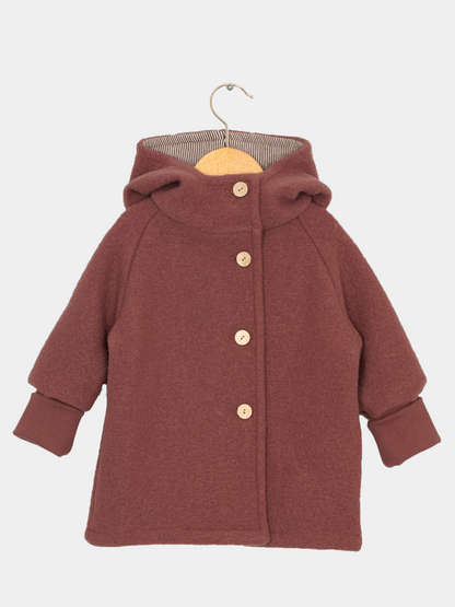 Wichteljacke Wollwalk - Ziegel: Kinder-Hoodie-Mantel aus weichem Wollstoff, mit geräumiger Kapuze, vier Holzknöpfen, breiten Rippbündchen und einem geraden Schnitt auf Holzbügel, ideal für Herbst bis Frühling.