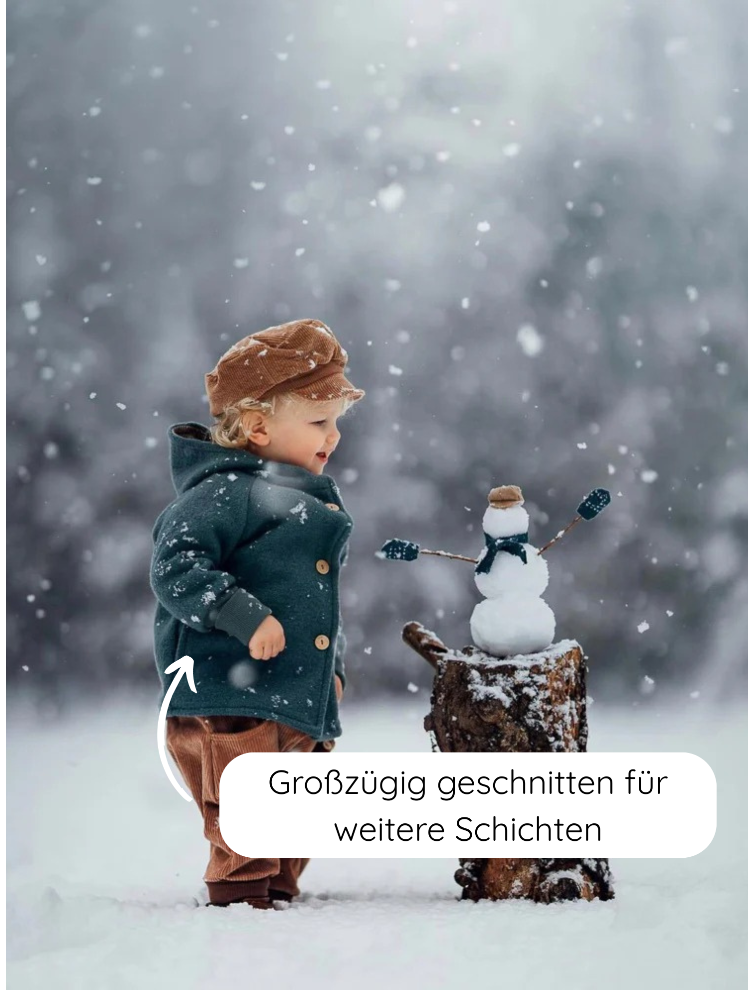 Ein Kleinkind im Schnee trägt die Wichteljacke Wollwalk - Taube mit Bio-Jersey-Futter, sieht einen kleinen Schneemann an. Die Jacke ist großzügig geschnitten für zusätzliche Lagen.