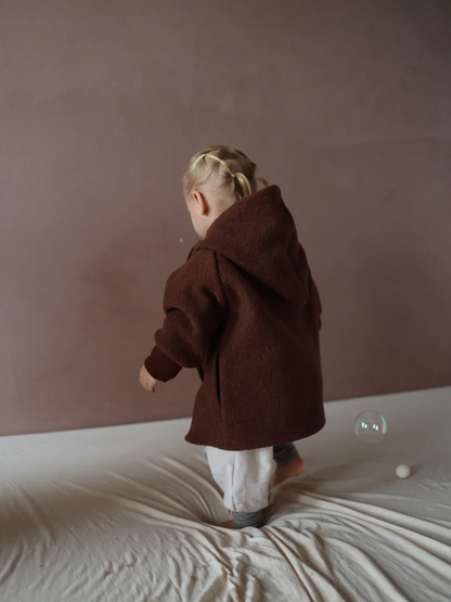 A child is wearing the Wichteljacke Wollwalk – Chocolate with Hood, made from high-quality boiled wool and perfectly lined. The jacket is ideal for several seasons and provides freedom of movement.