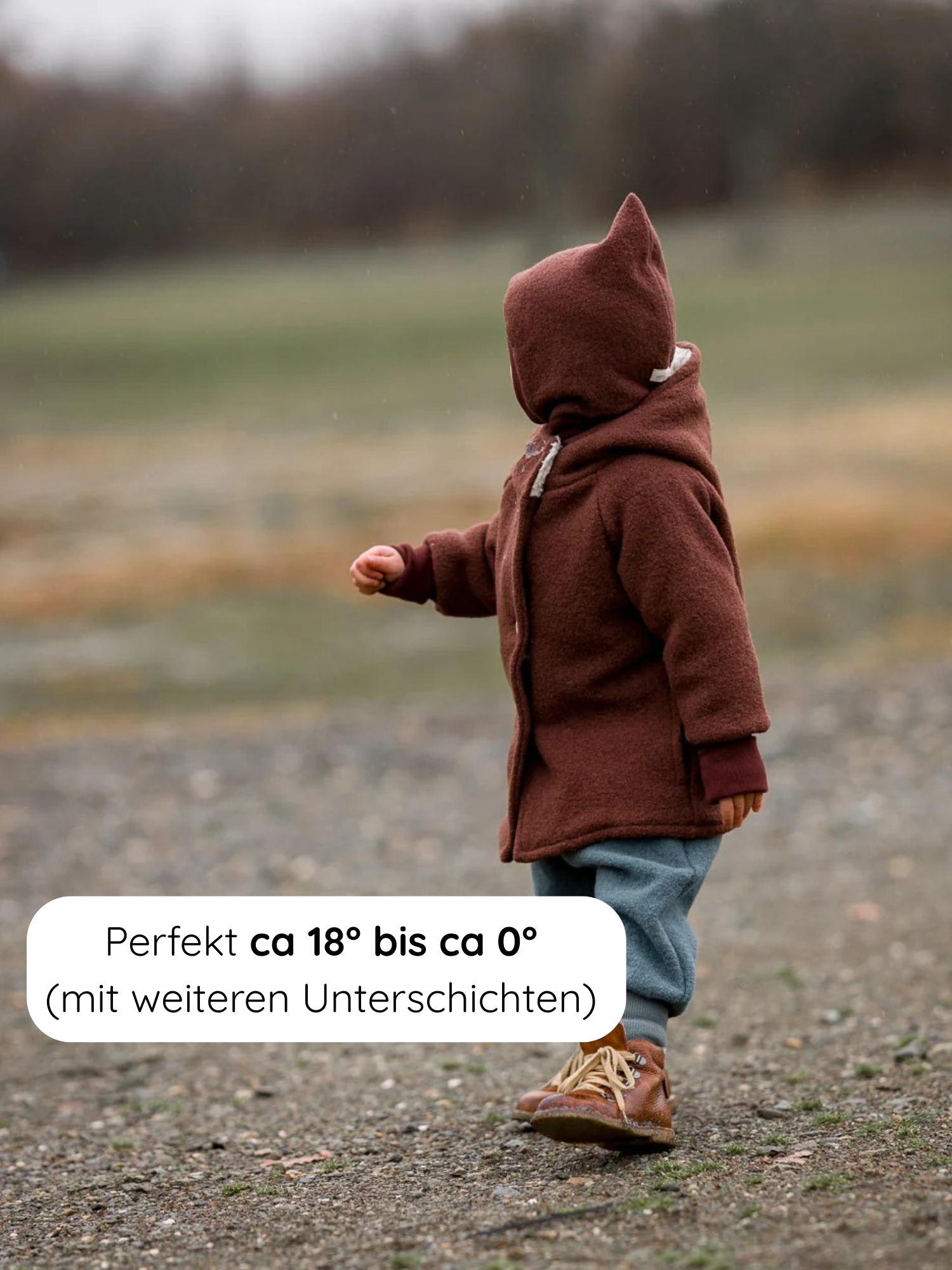 Wichteljacke Wollwalk - Schoko: Kleinkind trägt eine kastanienfarbene Wollwalk-Wichteljacke mit Kapuze, ausgestattet mit kleinen Ohren, ideal für Herbst bis Frühling, bietet Wärme und Bewegungsfreiheit bei Temperaturen von 18°C bis 0°C.