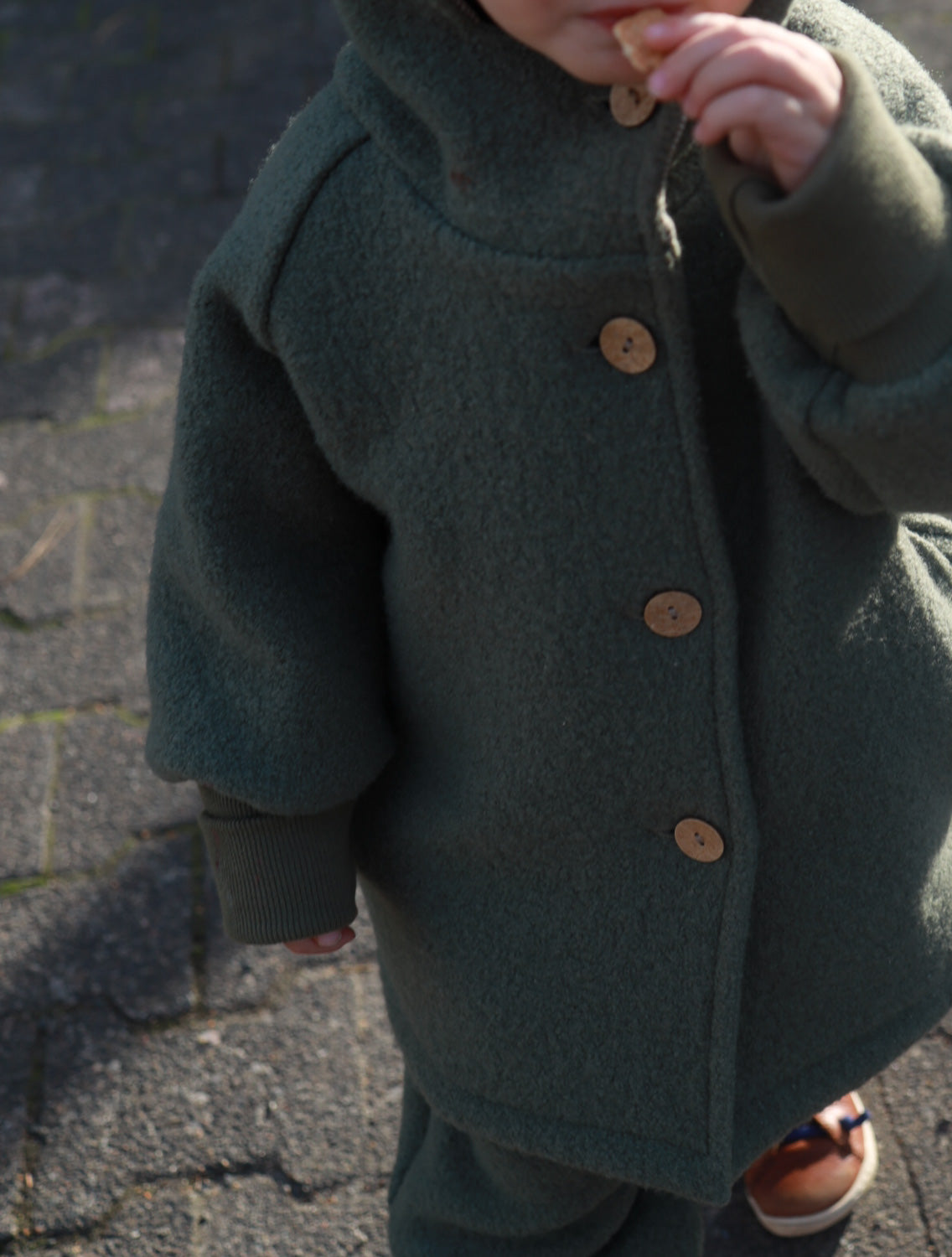 Kind trägt die Wichteljacke Wollwalk - Pistazie mit krempelbaren Bündchen, gefertigt aus hochwertigem Wollwalk, gefüttert mit Bio-Baumwoll-Jersey, ideal für Herbst bis Winter. nachhaltige Kinderkleidung aus Wollwalk